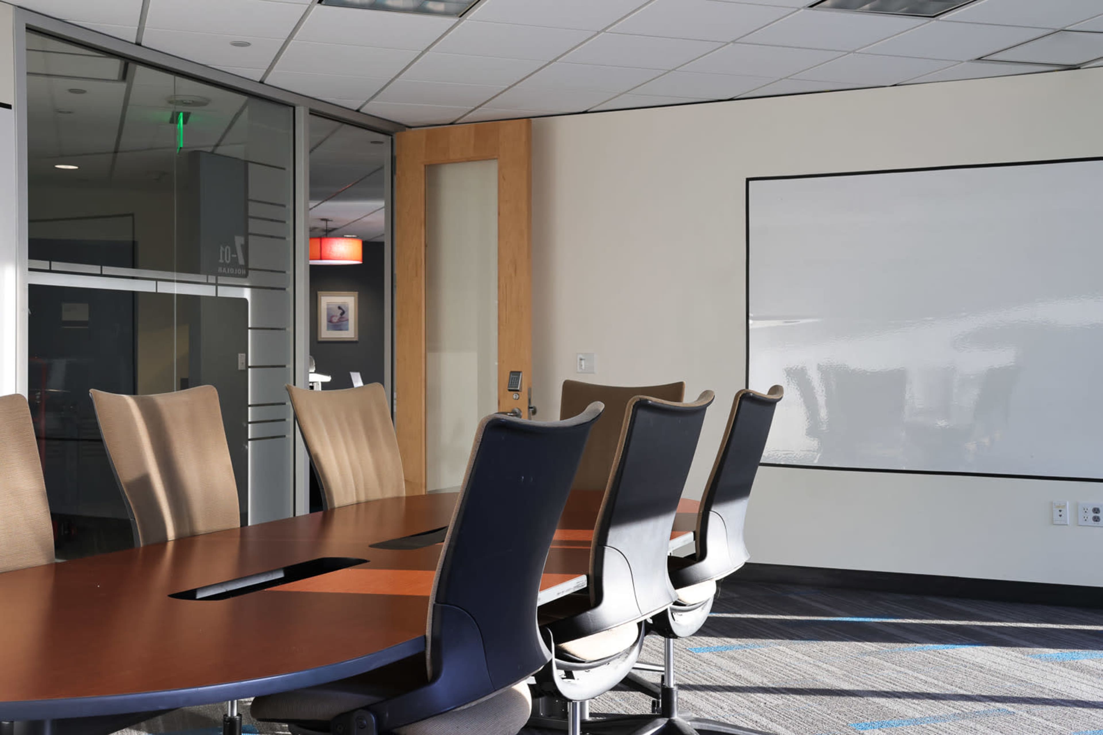 The image shows a conference room with a long wooden table, several office chairs around it, and a large whiteboard mounted on the wall.