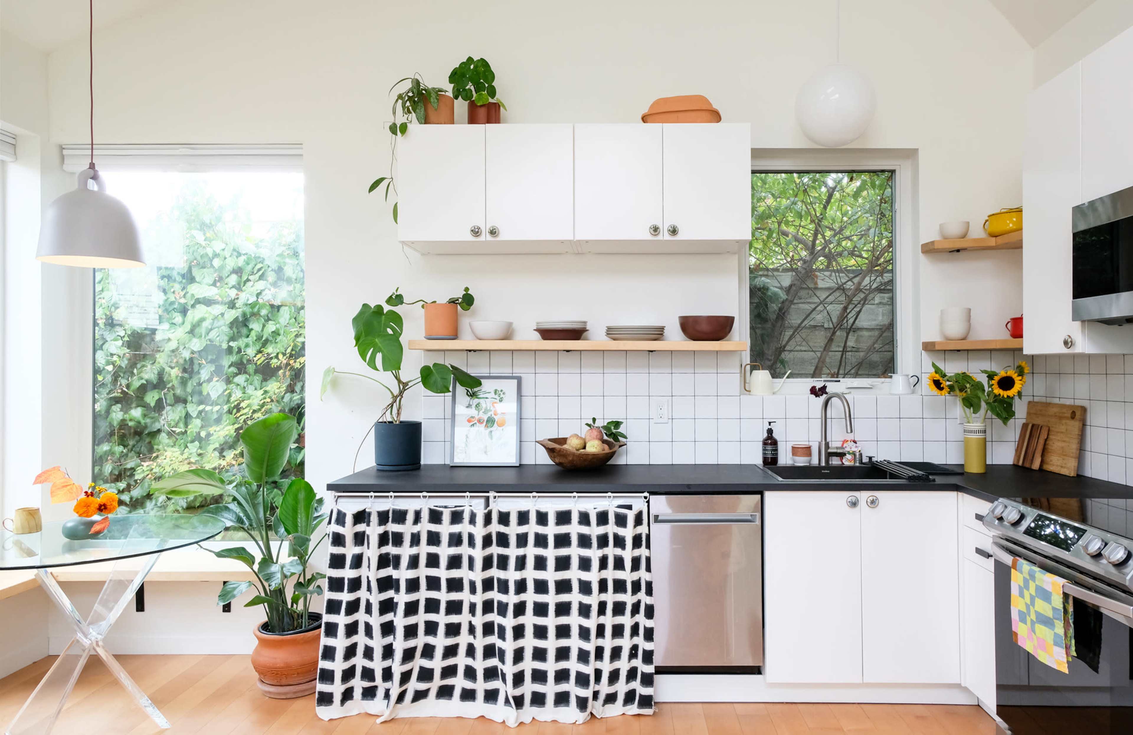 A bright kitchen features white cabinets, a black countertop, and an array of plants and decorative items on display.