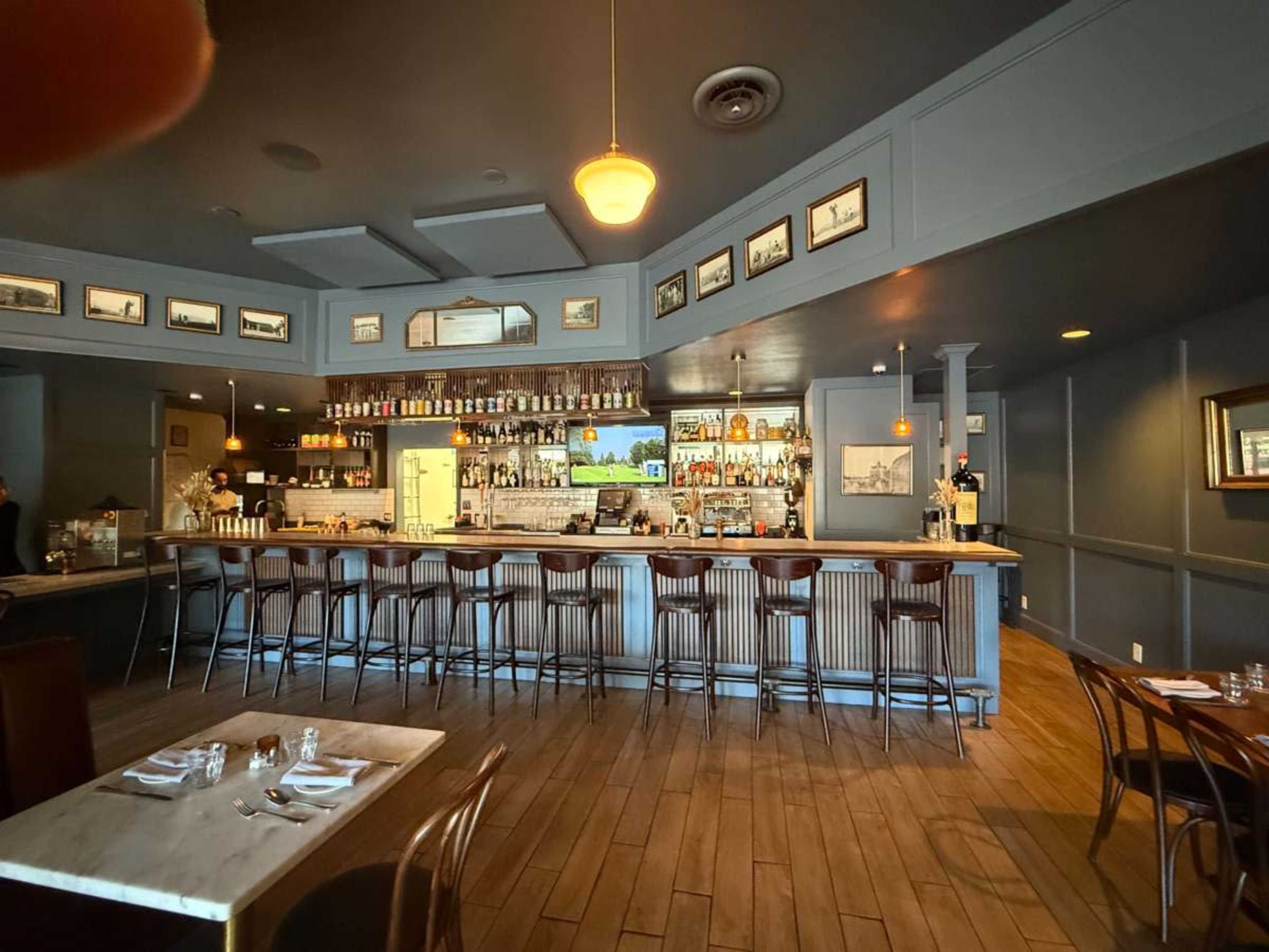 The image shows a dimly lit restaurant bar area with a marble countertop, tall wooden stools, and framed pictures on the walls.