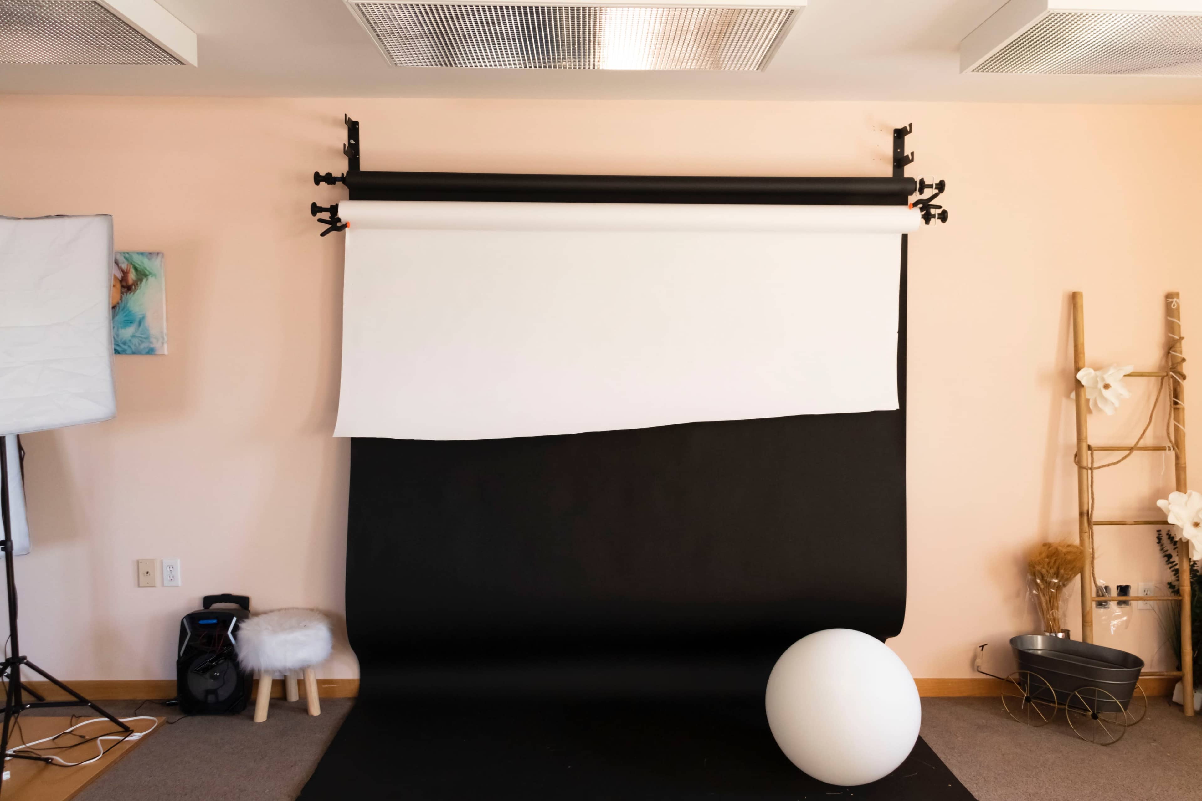 A photography studio features a black and white backdrop setup, accompanied by a round white object and a small stool.