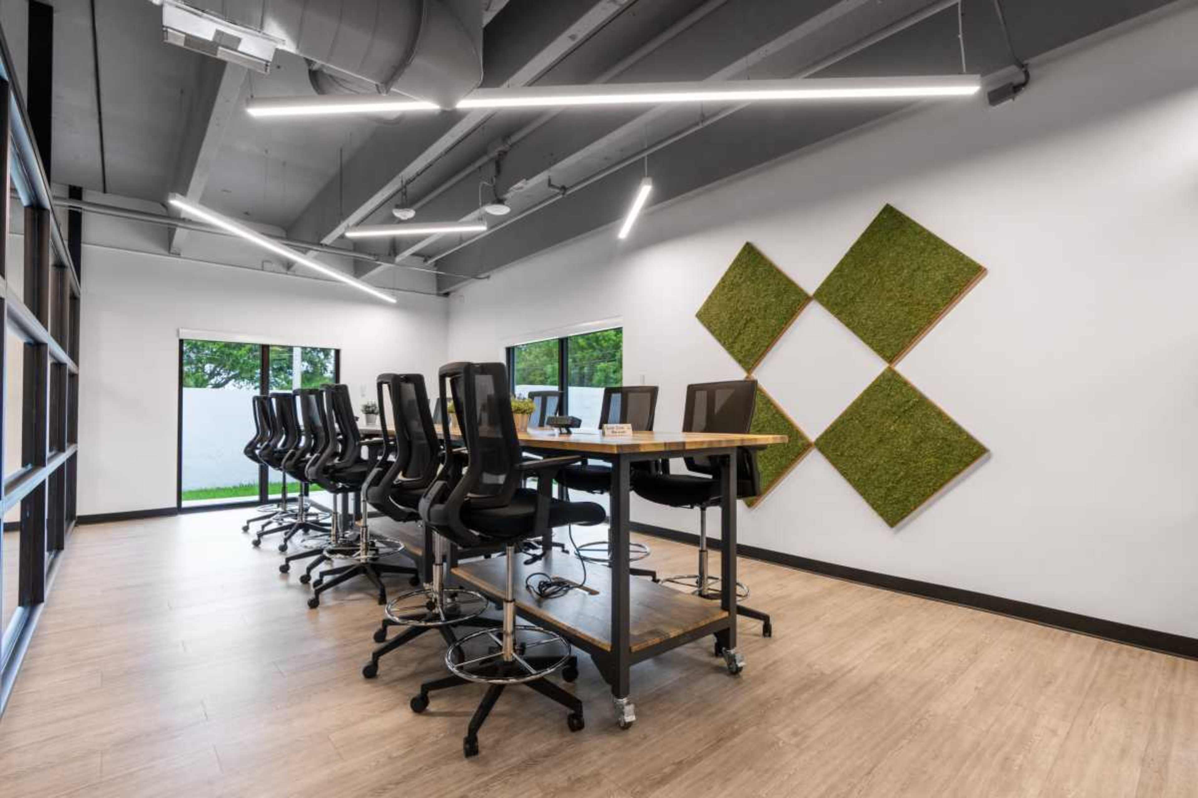 A modern conference room features a long wooden table with high-backed chairs and decorative wall-mounted greenery.