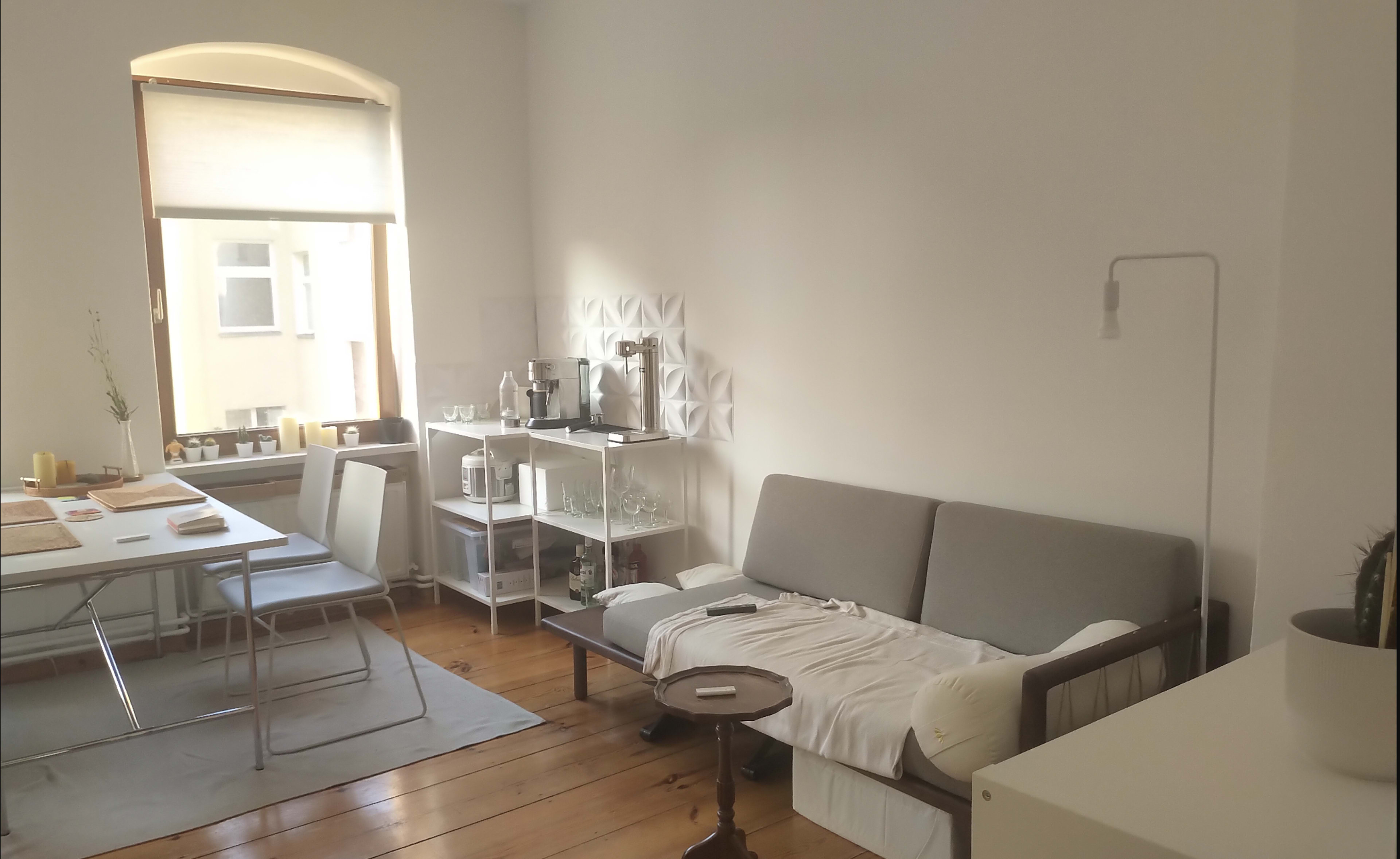 A living space features a gray sofa, a wooden table with chairs, and a window allowing natural light to enter.
