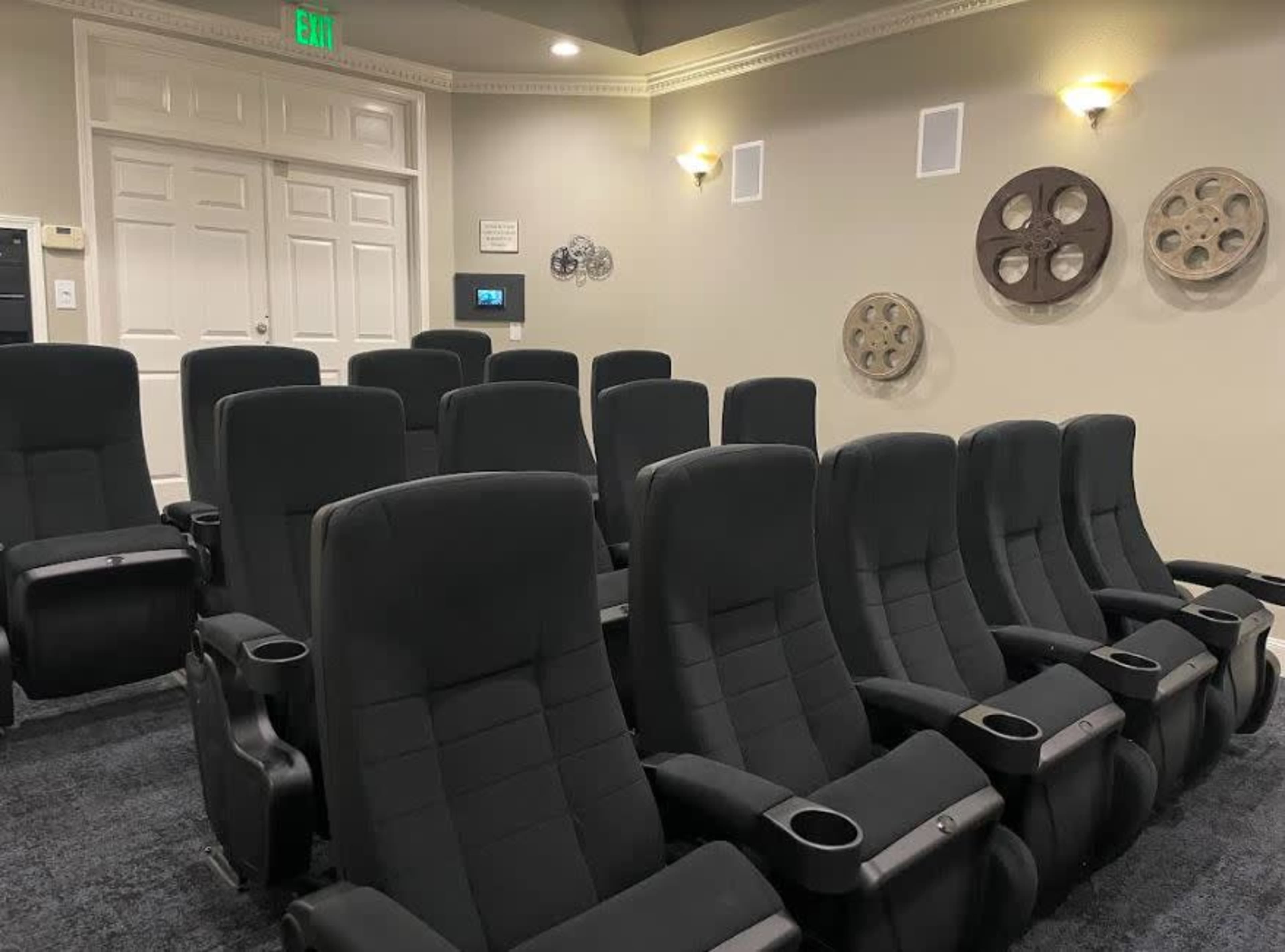 A small home theater room with several black reclining chairs arranged in rows, along with film reels displayed on the walls.