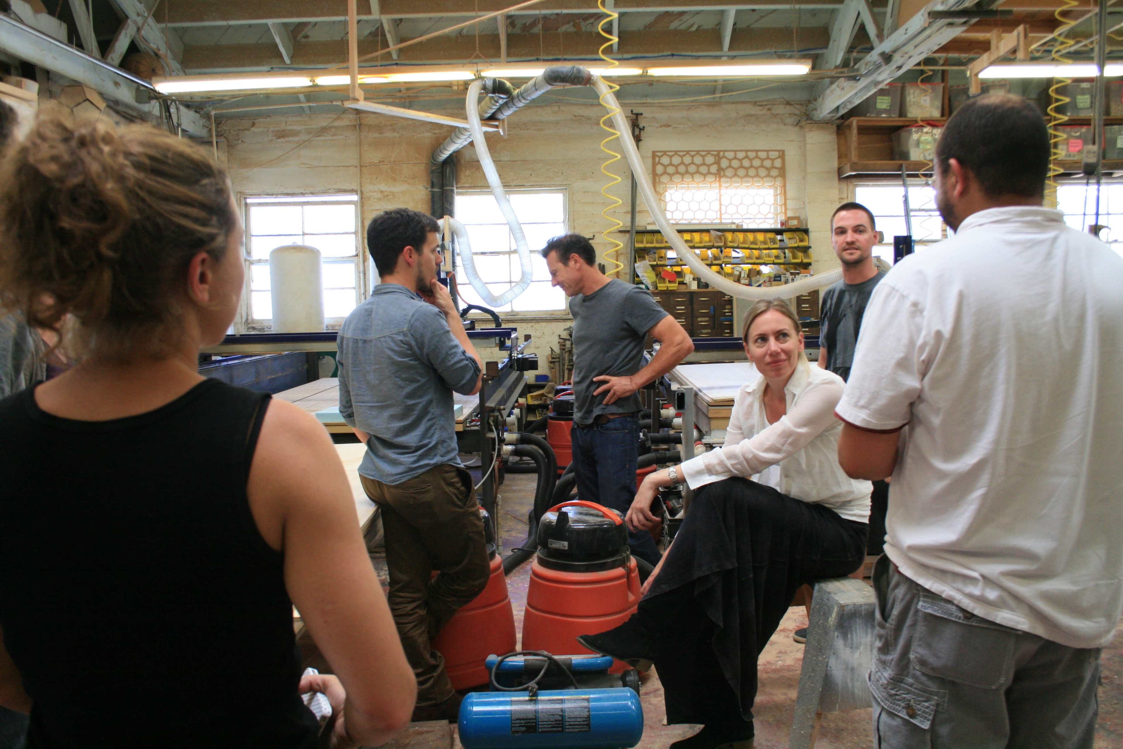 A group of five people interacts inside a workshop filled with tools and equipment.
