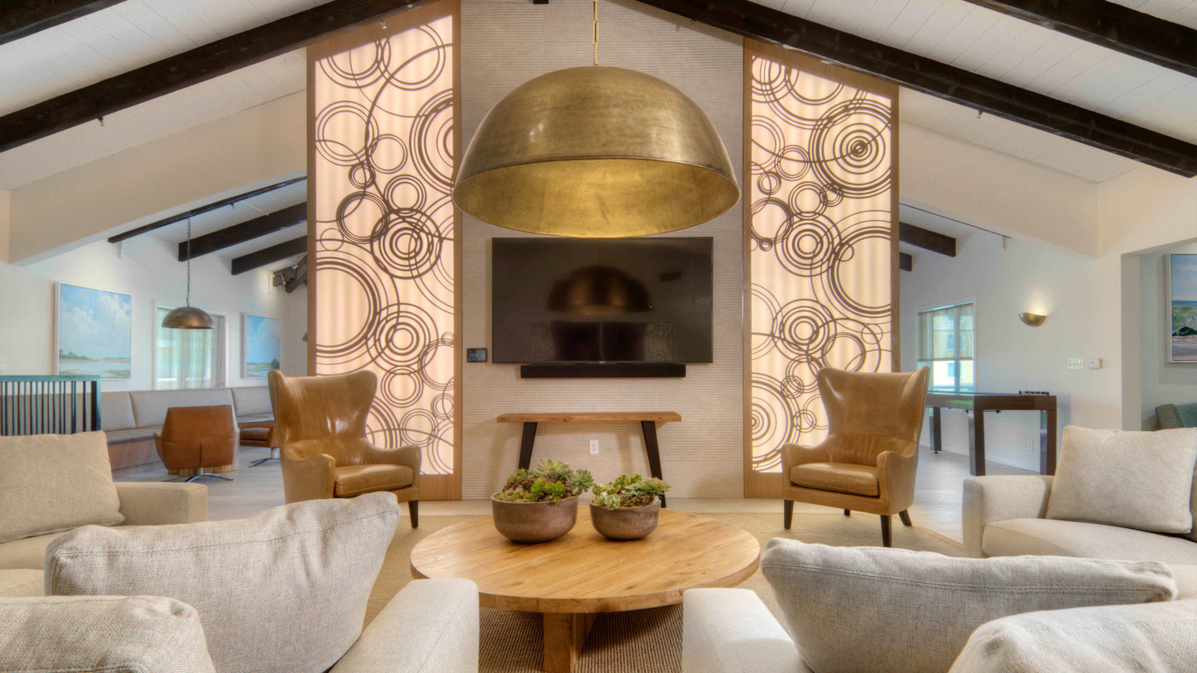 A modern living room featuring two large, patterned wall panels, a flat-screen TV, a wooden table with potted plants, and comfortable seating arrangements.