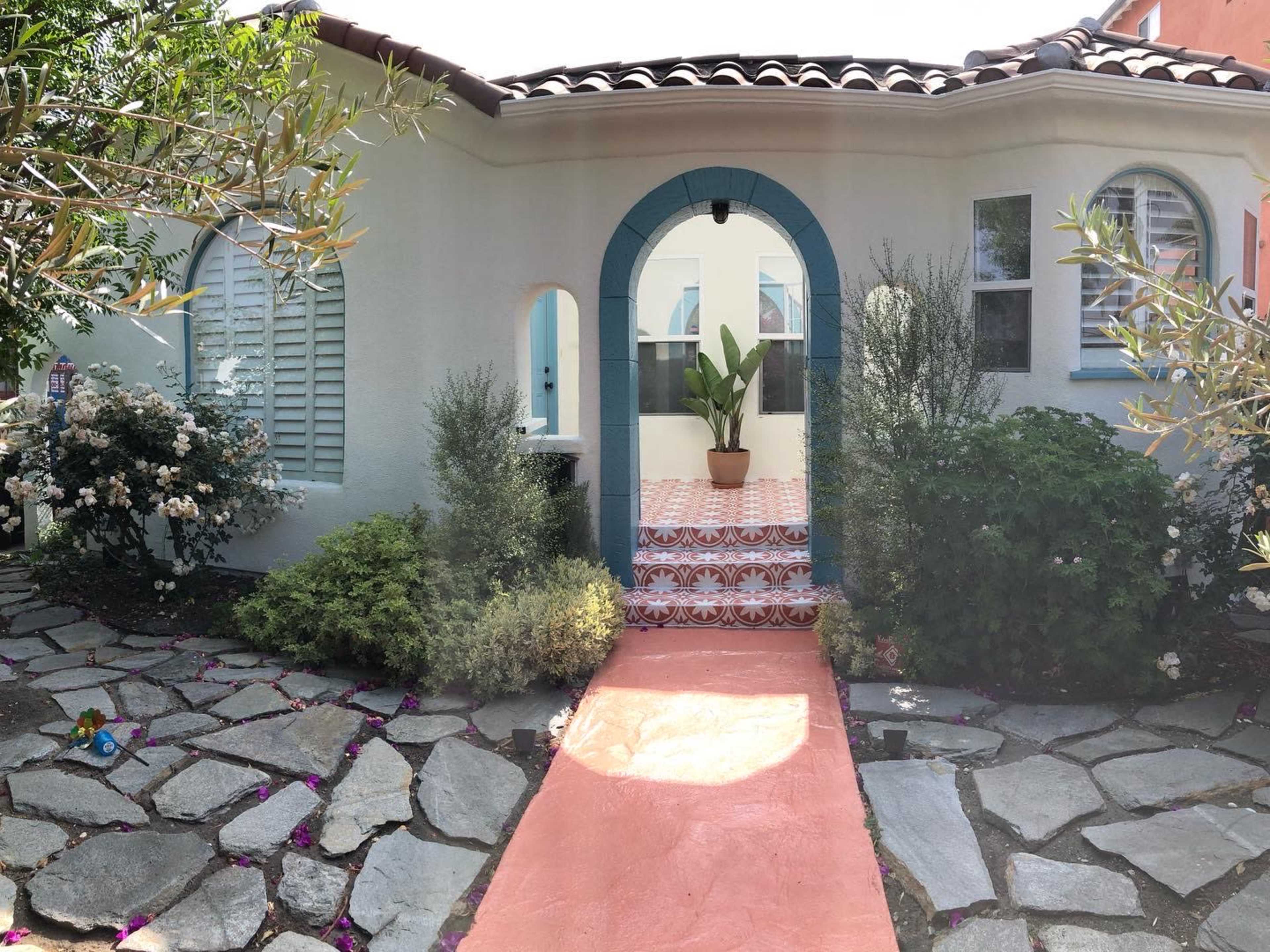 A quaint house with a tiled entrance, surrounded by colorful flowers and stone pathways.