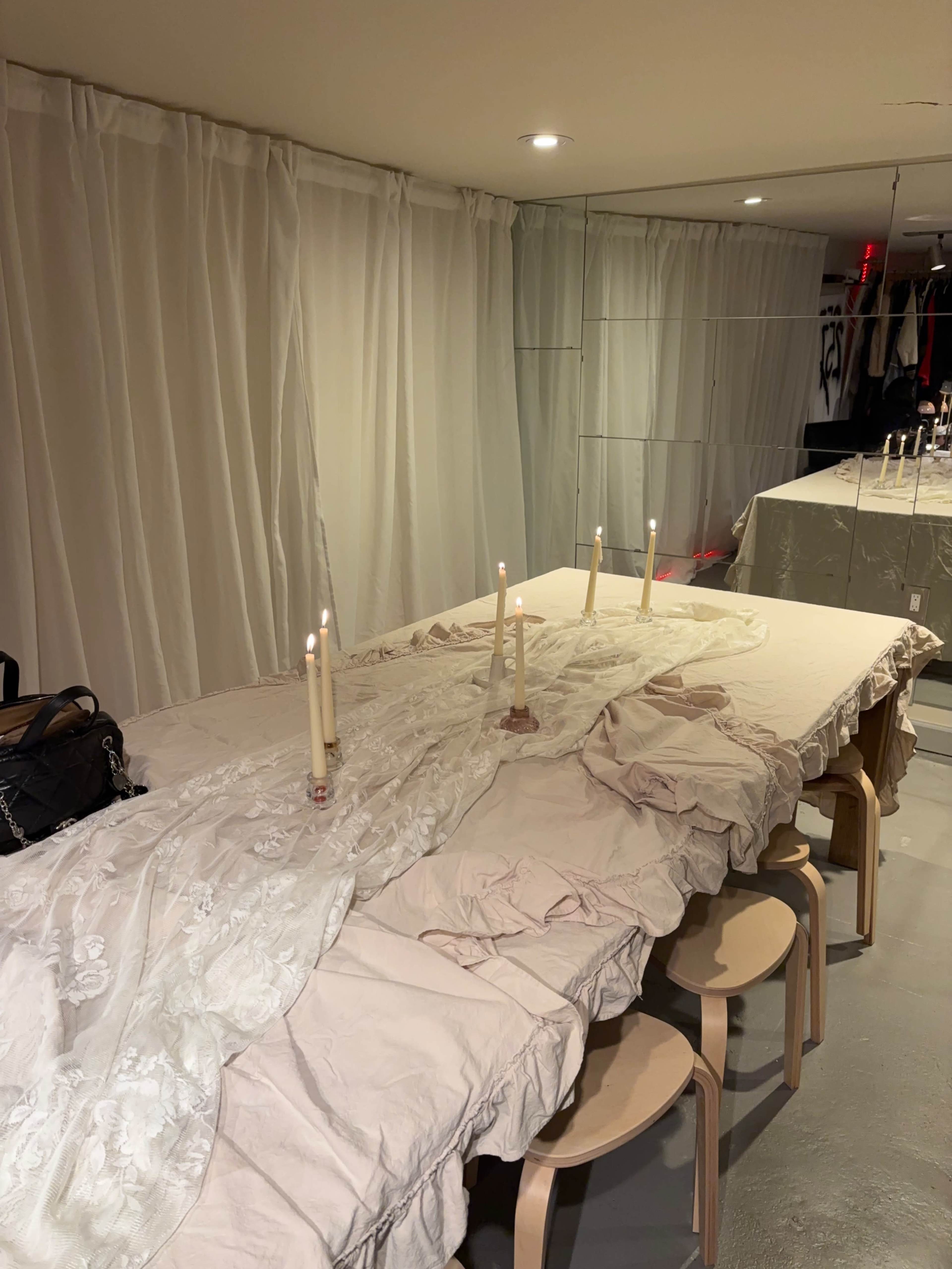 A long table is set with lit candles and covered with fabric in a softly lit room featuring mirror walls.