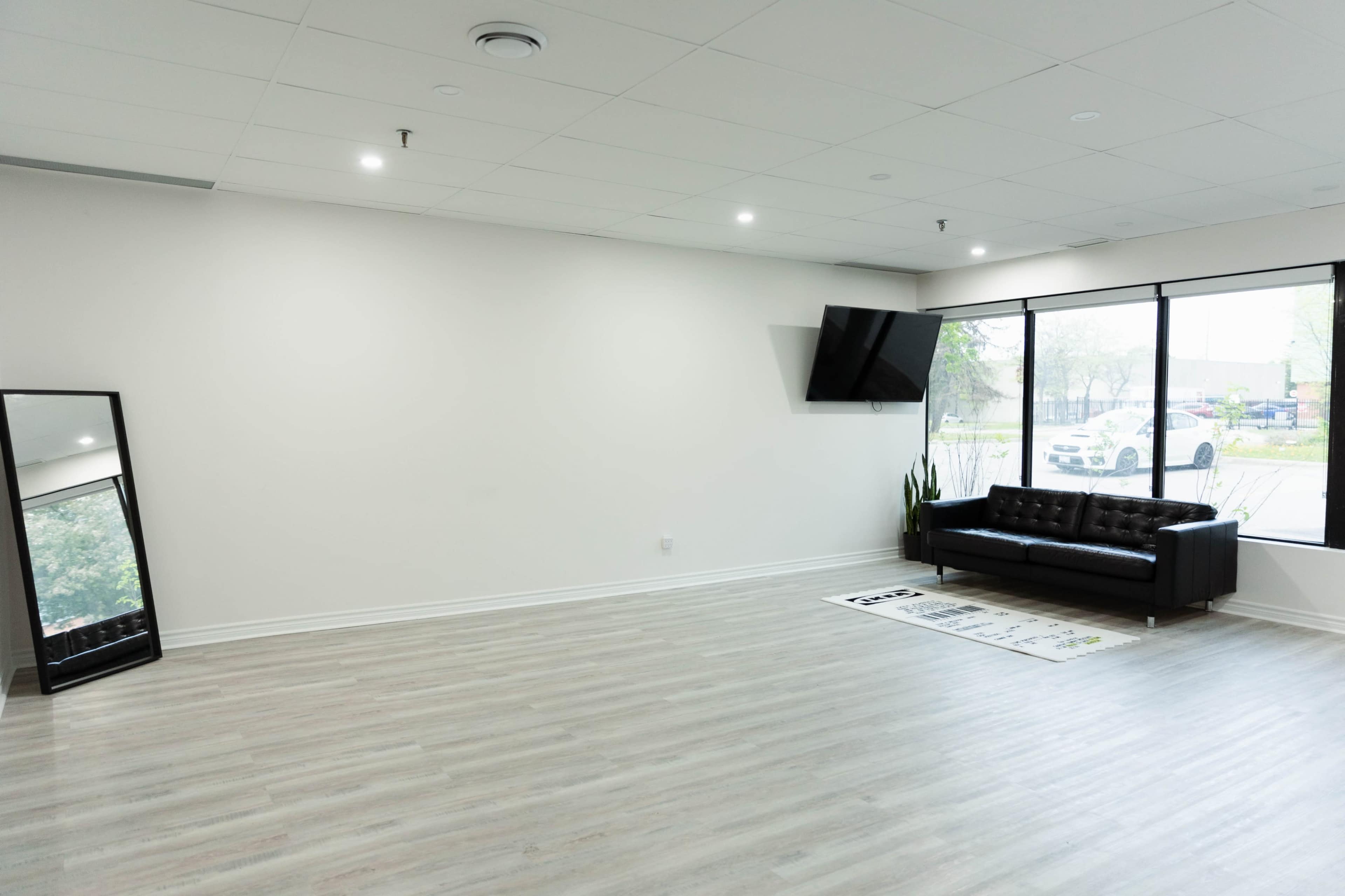 A spacious, empty room with a black couch, a large mirror, and a television mounted on the wall.
