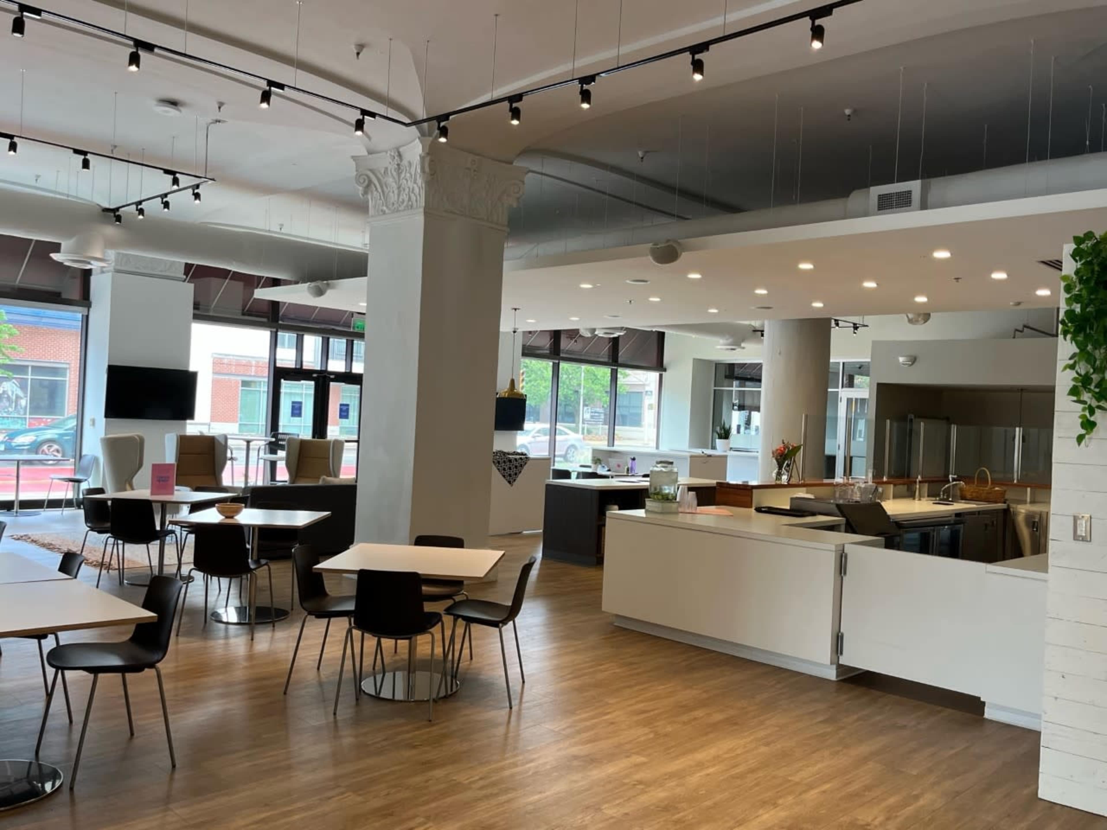 A modern, open interior space with dining tables, chairs, and a kitchenette area featuring stainless steel appliances.