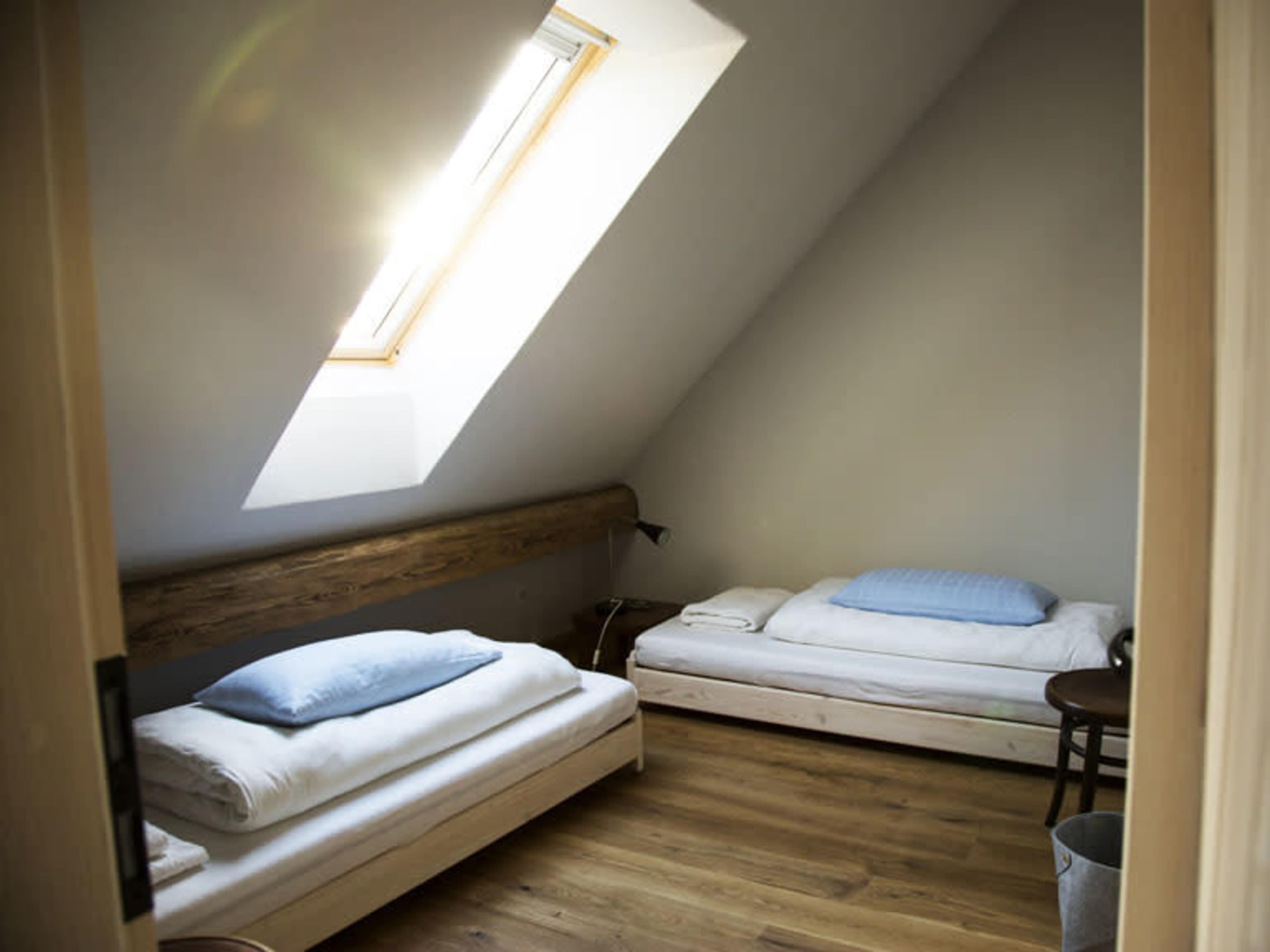 A cozy attic room with two single beds, a skylight, and wooden floors.