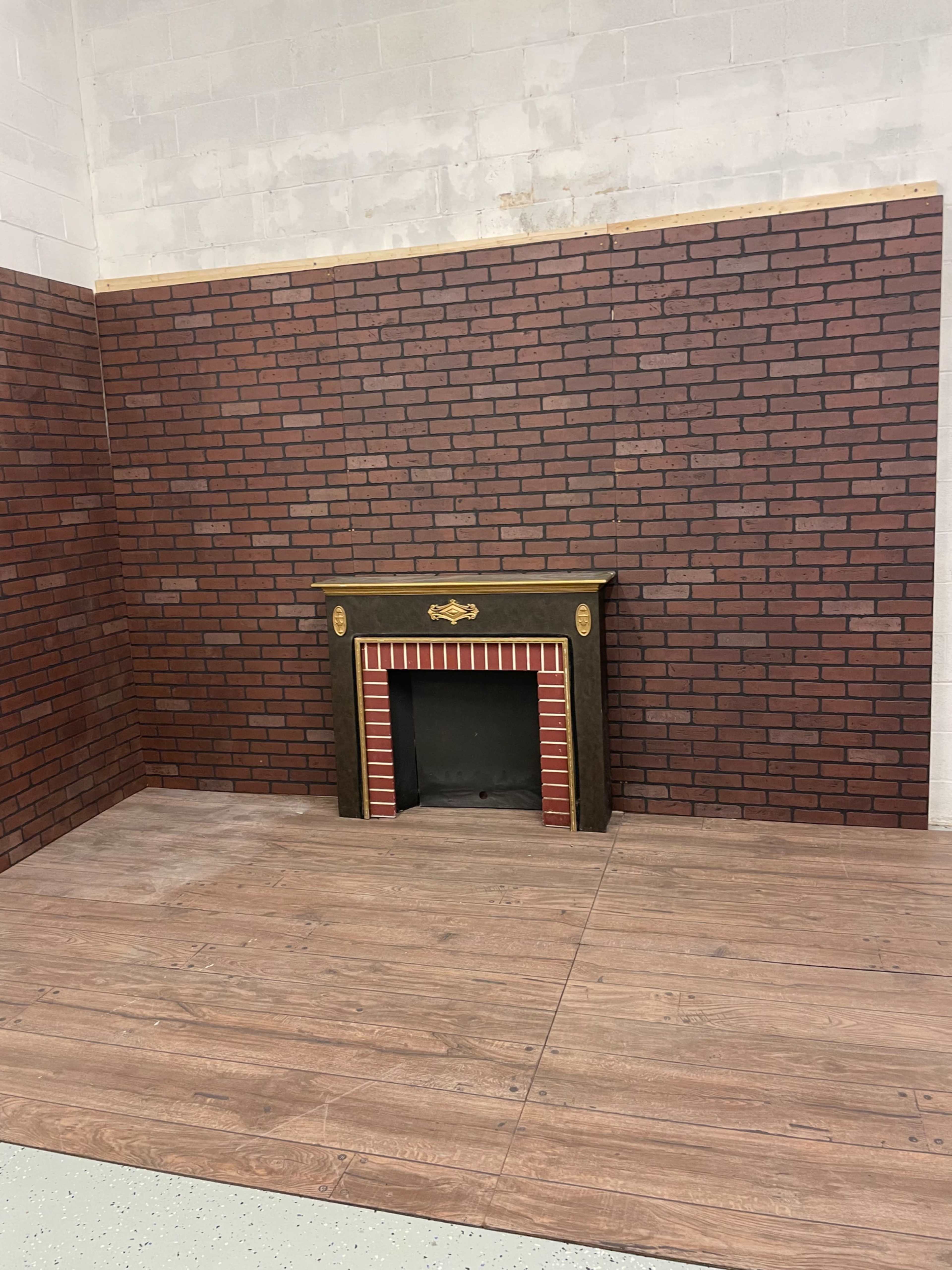 The image shows an empty corner of a room featuring a brick-patterned wall and a decorative fireplace installed against it.
