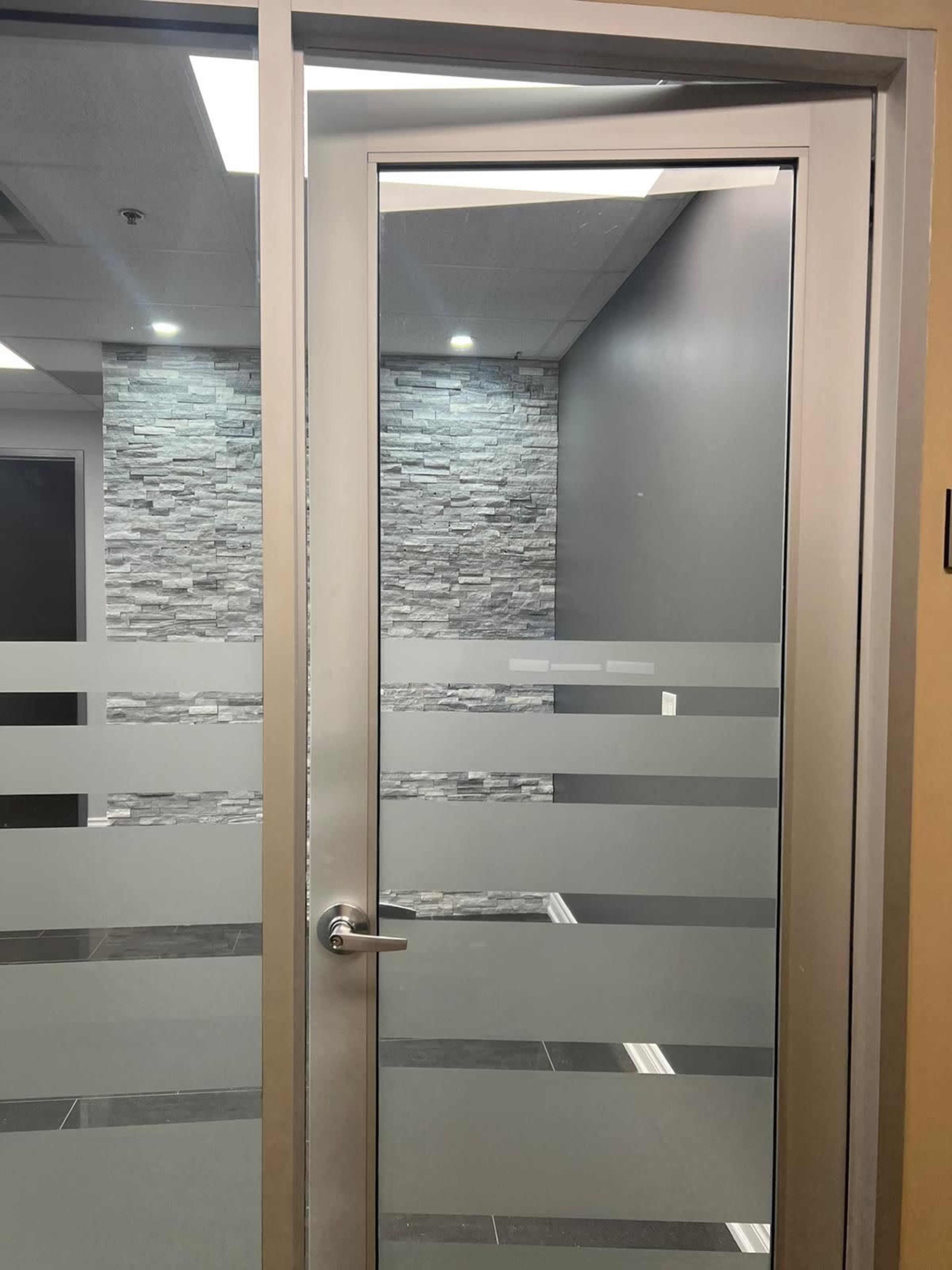 A glass door with horizontal frosted stripes, leading to a room with stone wall accents and neutral-colored walls.