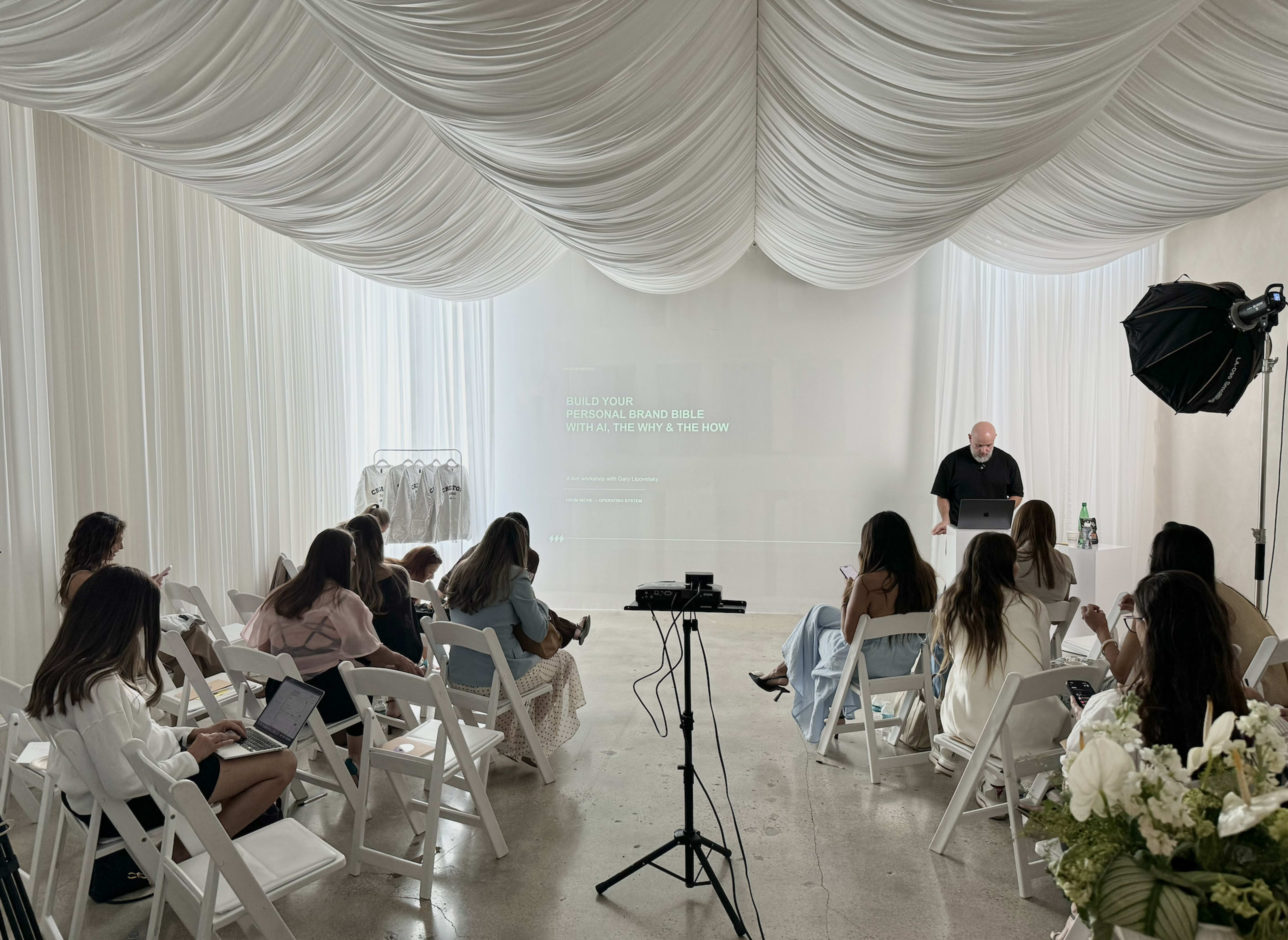 A presenter speaks to a seated audience in a softly lit, draped room during a personal branding workshop.