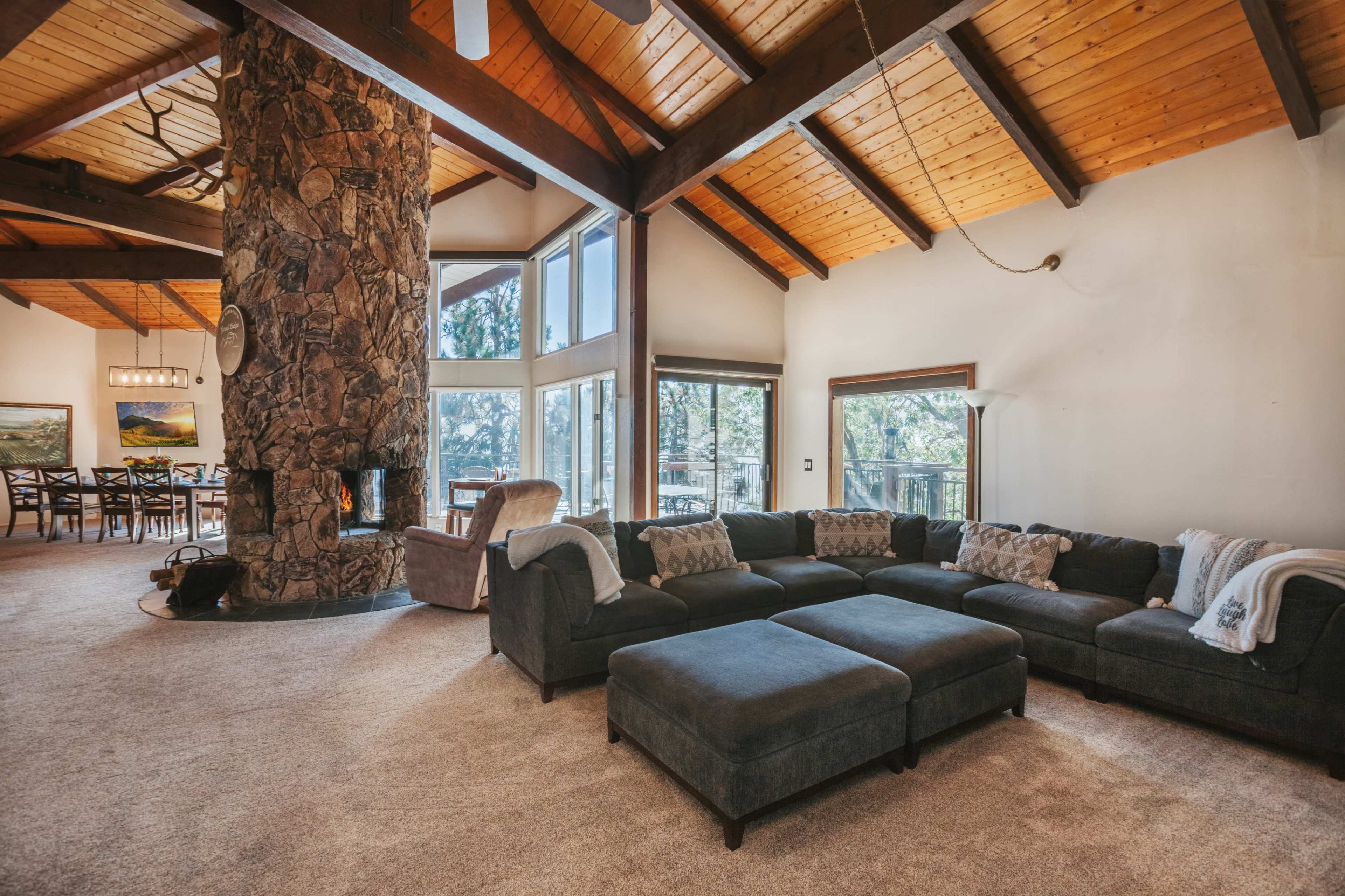 A spacious living room featuring a large sectional sofa, a stone fireplace, and high, wooden-beamed ceilings.