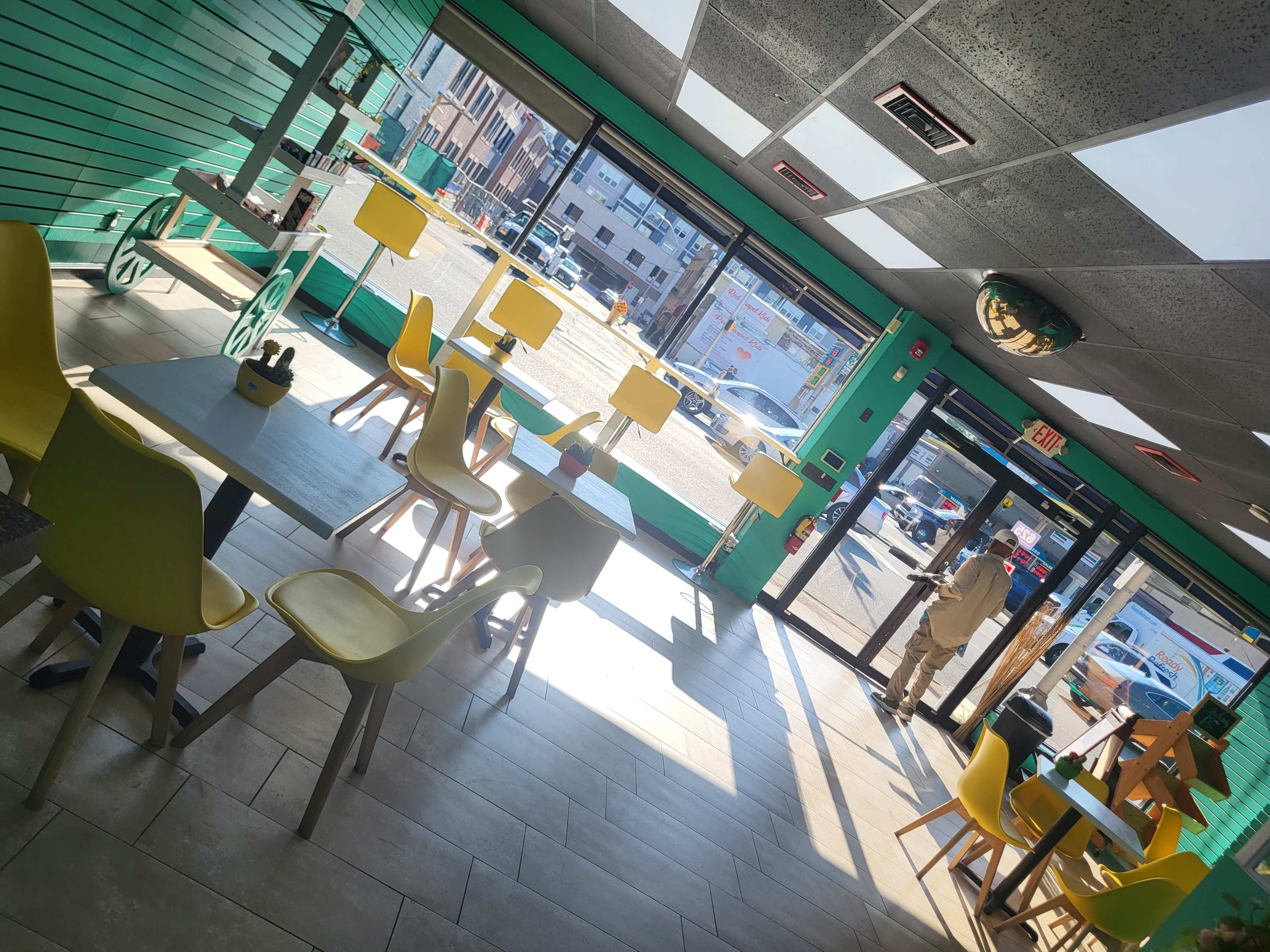 A brightly lit café interior with yellow chairs and tables, looking out through large windows onto a street scene.