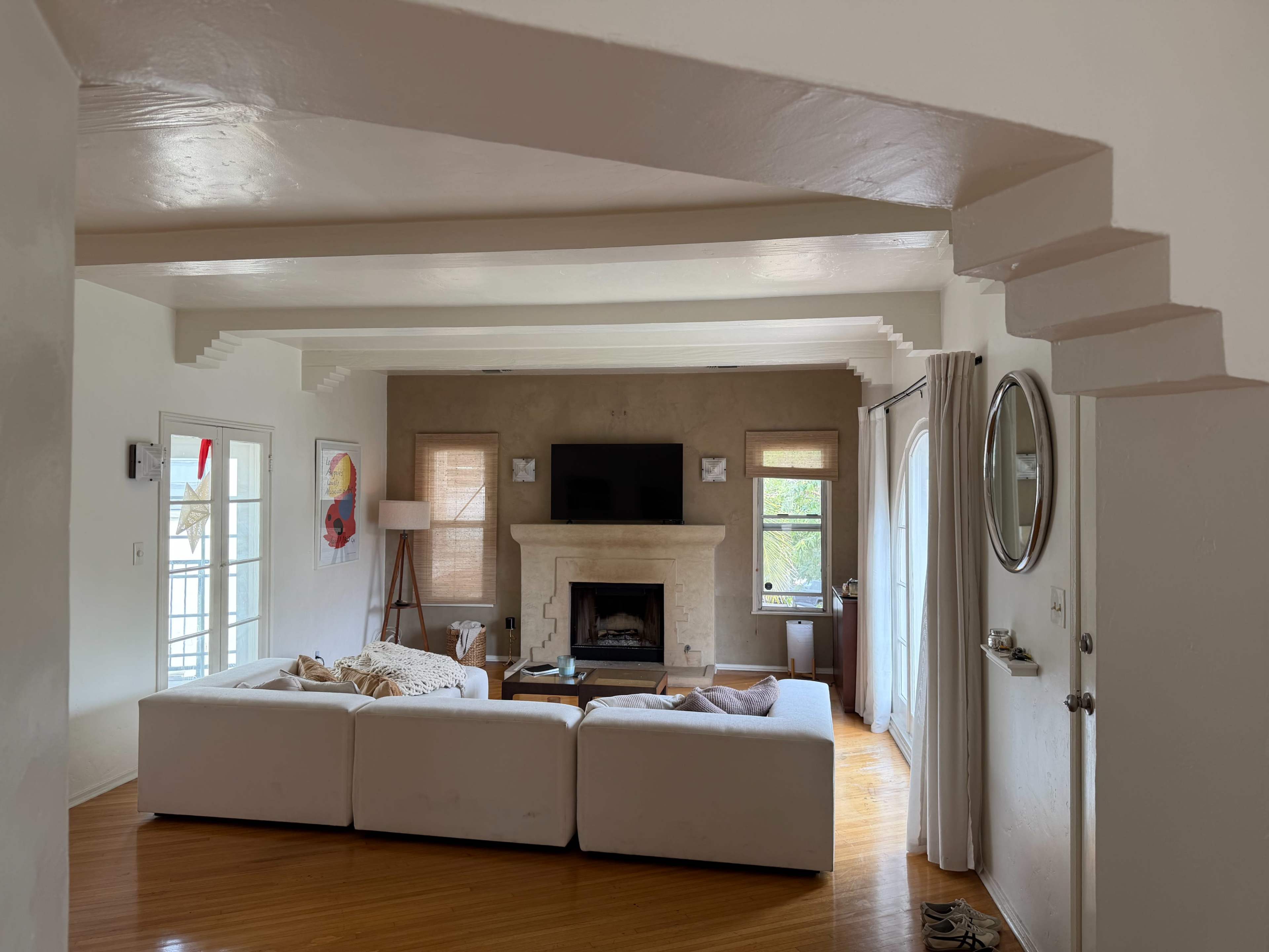The image shows a modern living room with a white sectional sofa, a stone fireplace, and large windows allowing natural light to enter.