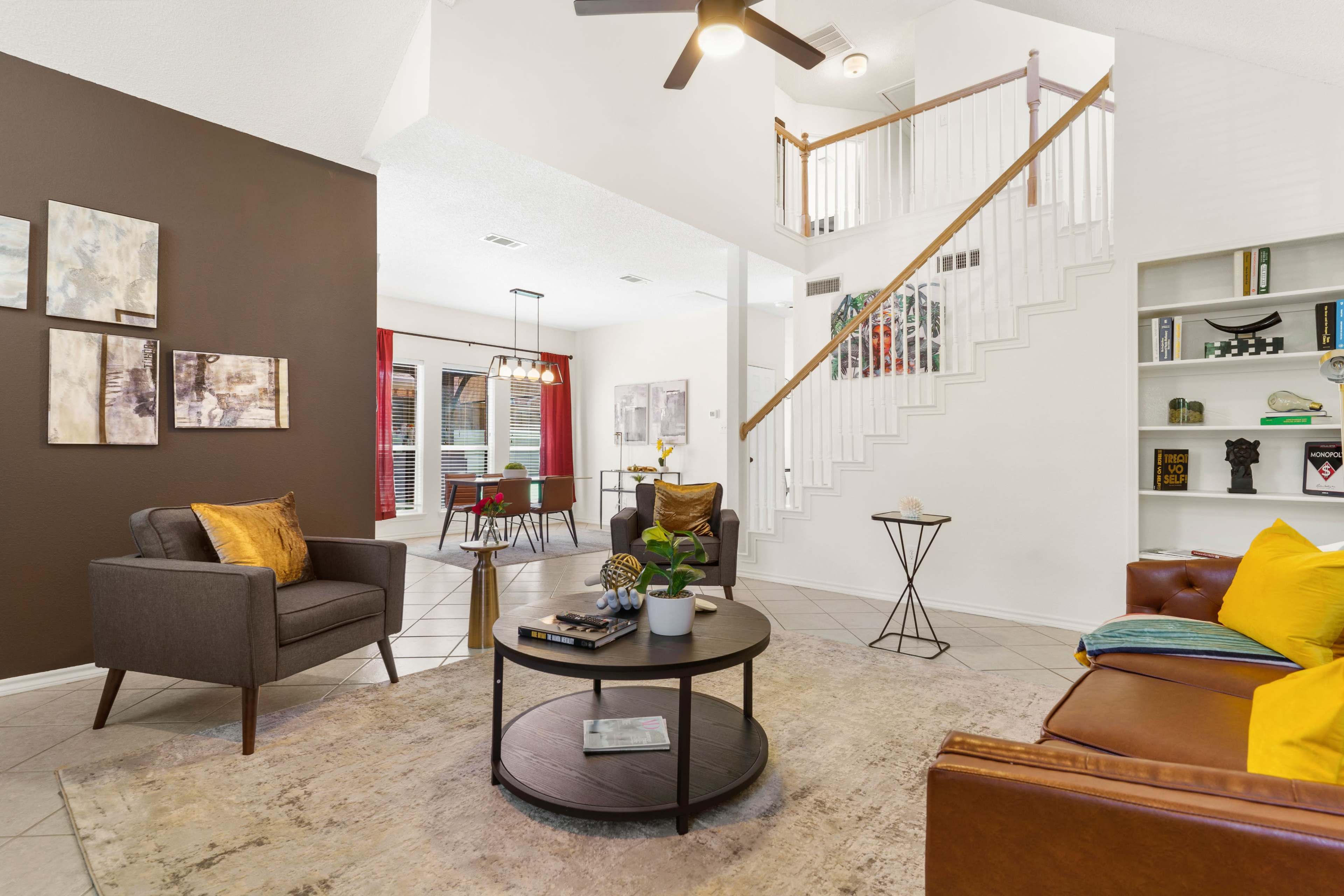 A modern living room with two seating areas, a round coffee table, and a staircase leading to an upper level.