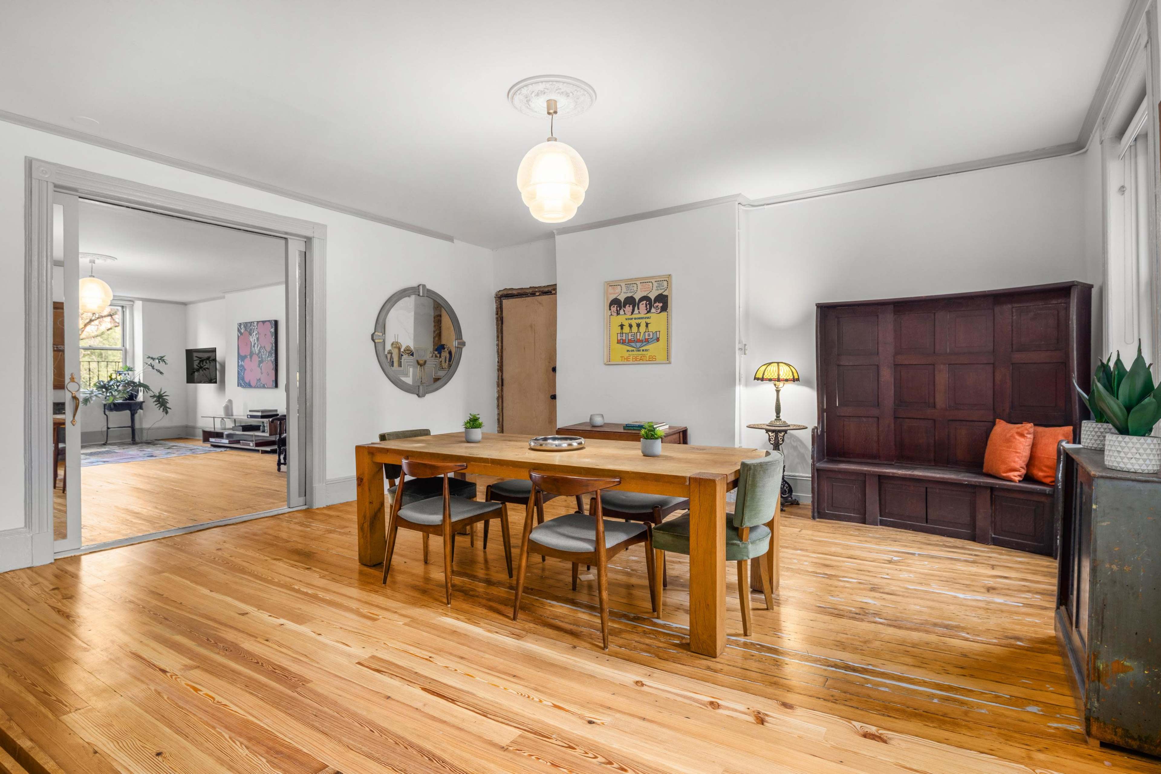 A dining area with a wooden table surrounded by chairs, a wall-mounted mirror, and a bench against the side, all featuring hardwood floors and a light fixture overhead.
