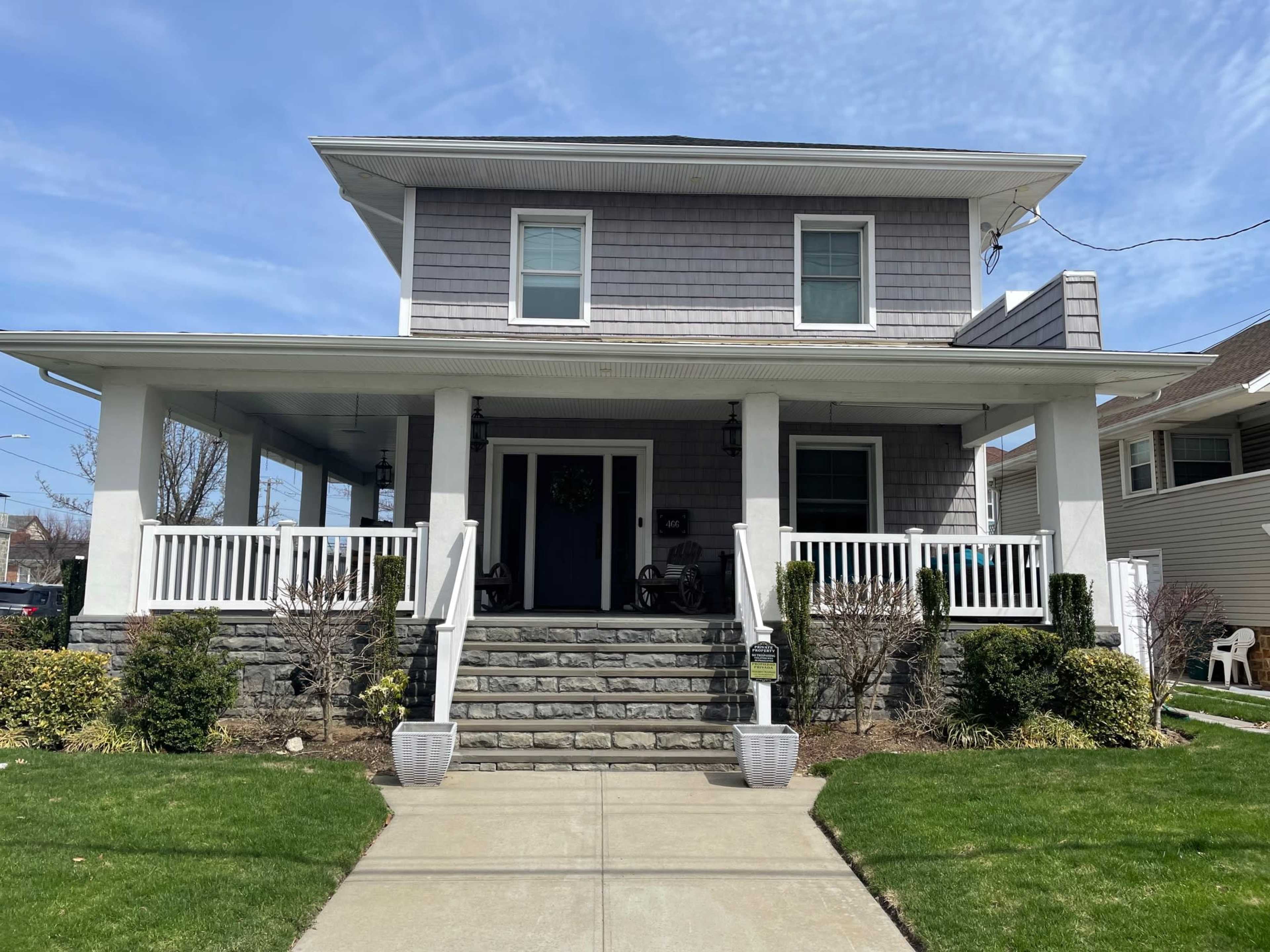 The image shows a two-story house with a gray shingle exterior, white trim, and a stone staircase leading to the front porch.