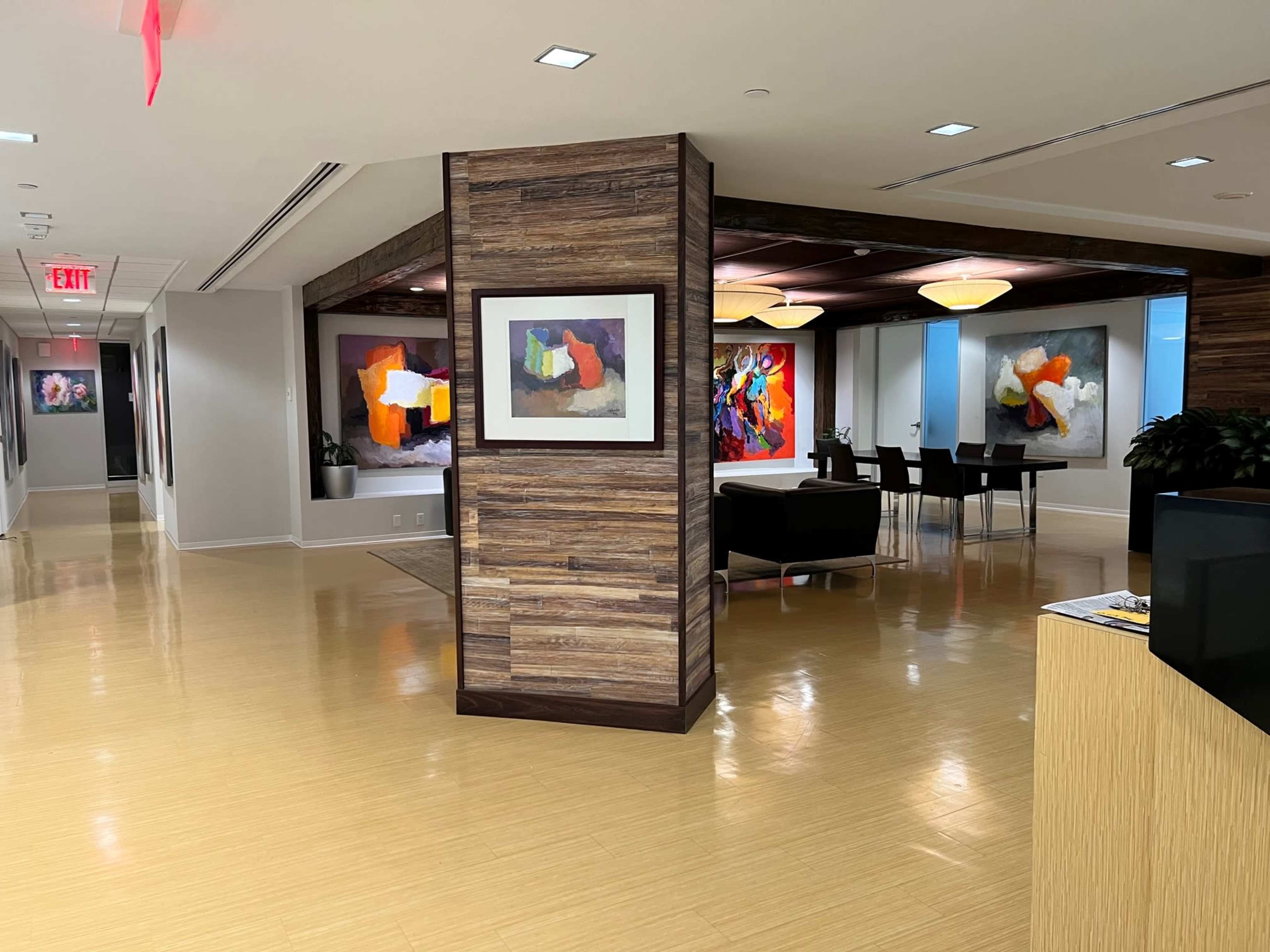 A modern office space featuring a wooden-columned partition, colorful abstract paintings on the walls, and a dining area with black furniture.