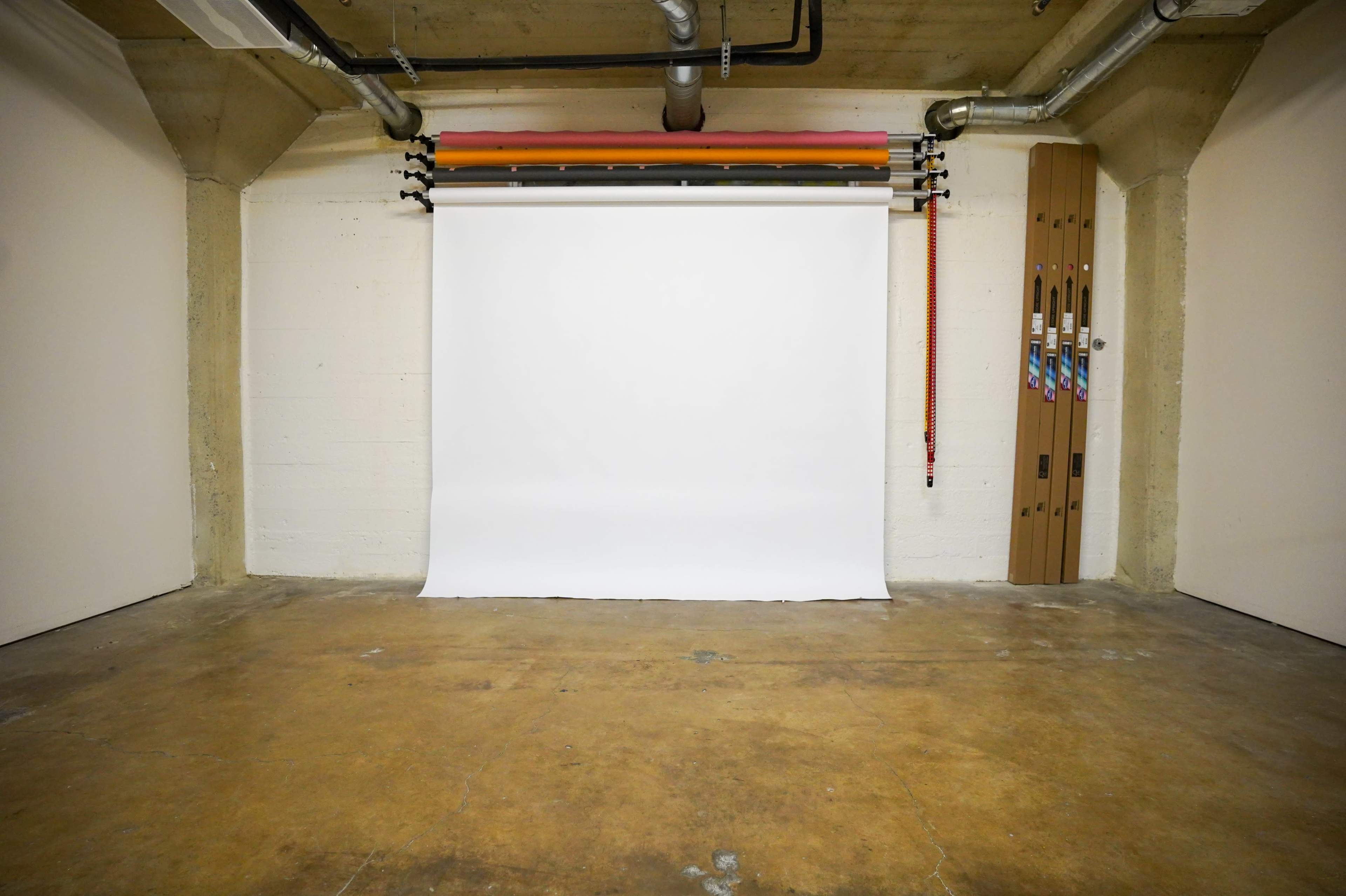 A bare studio space with a white backdrop, concrete walls, and a wooden rack holding various tools or equipment.