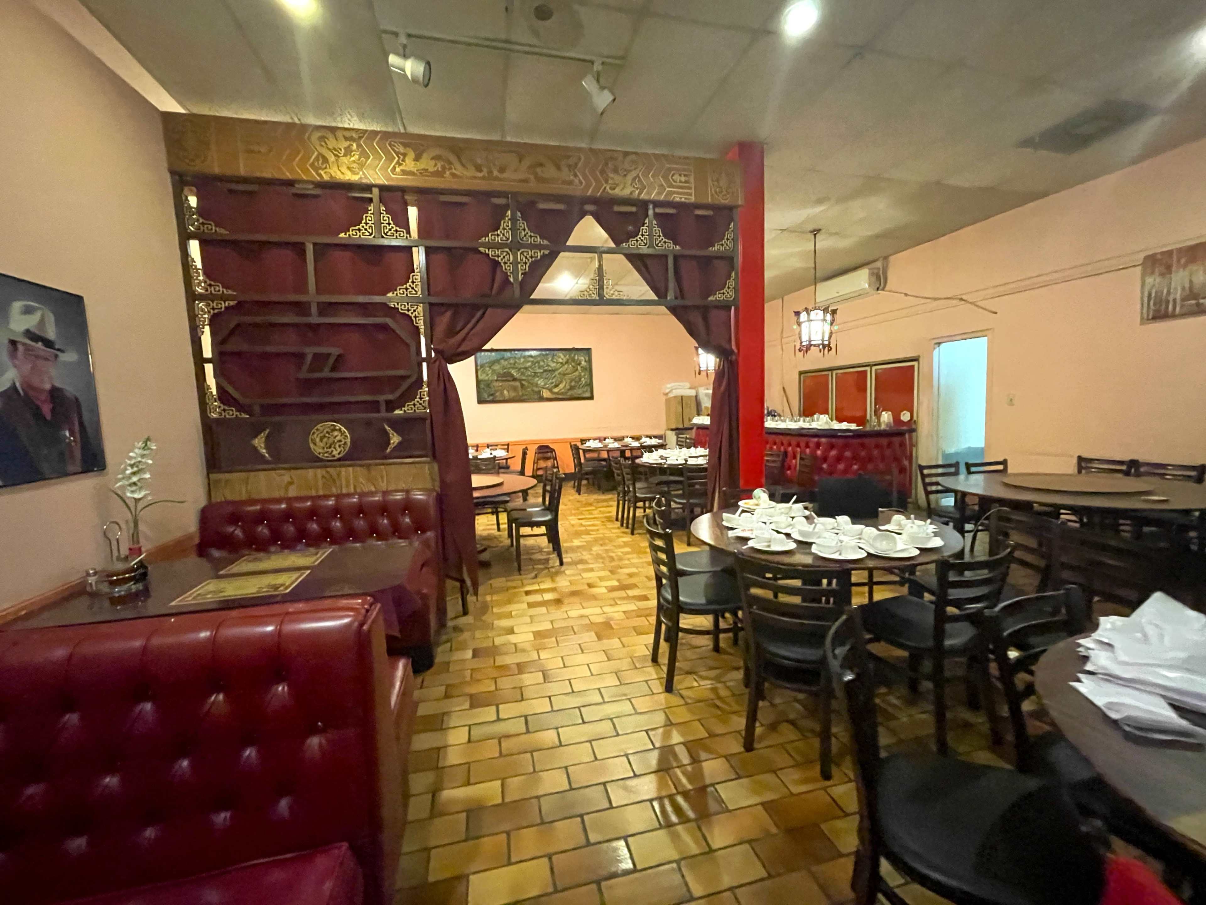 The image shows a restaurant interior with red leather seating, wooden tables, and a decorative partition featuring intricate designs.