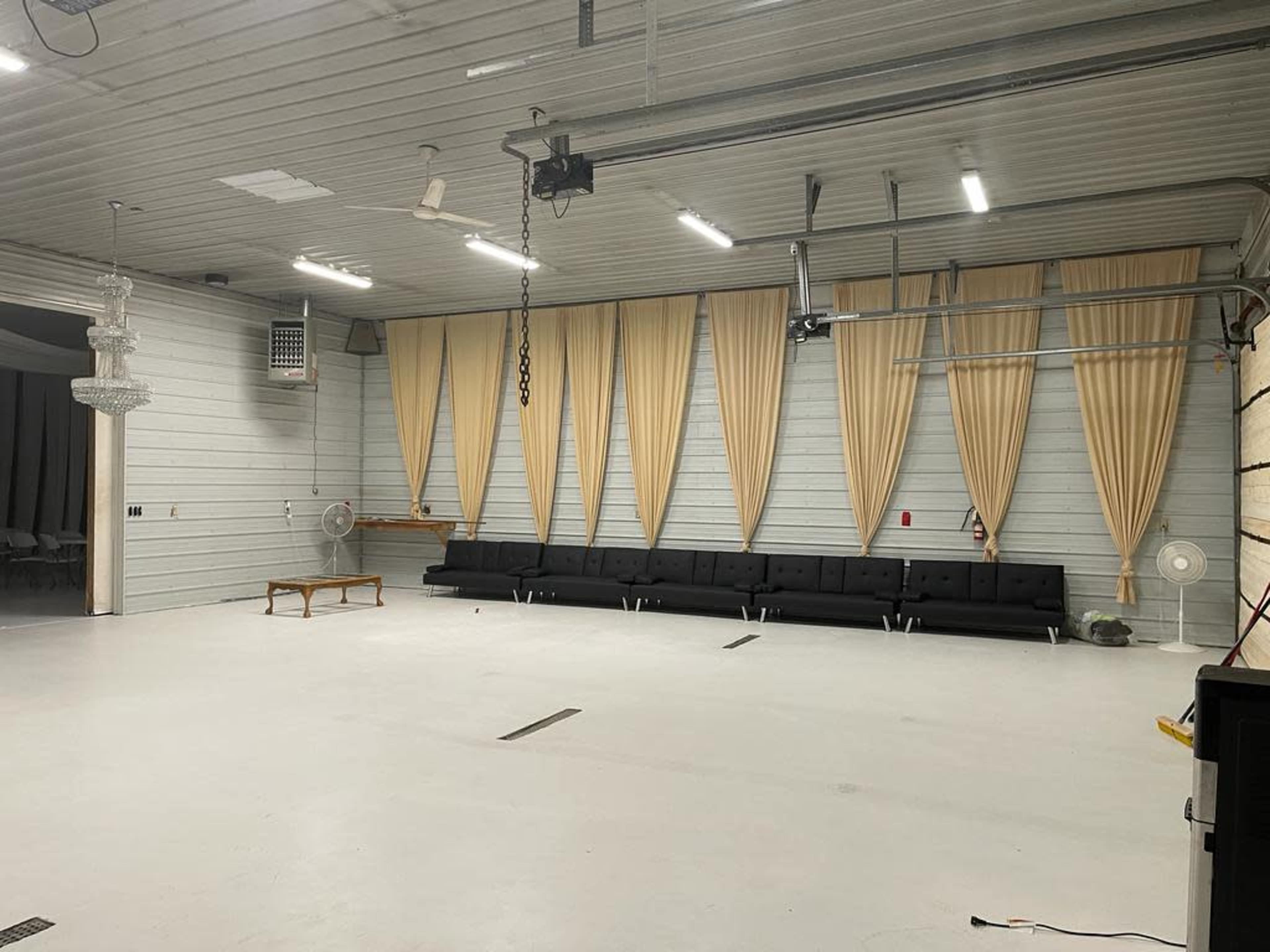 The image shows an empty interior space with a black sofa, beige curtains, and a white floor under overhead lighting.