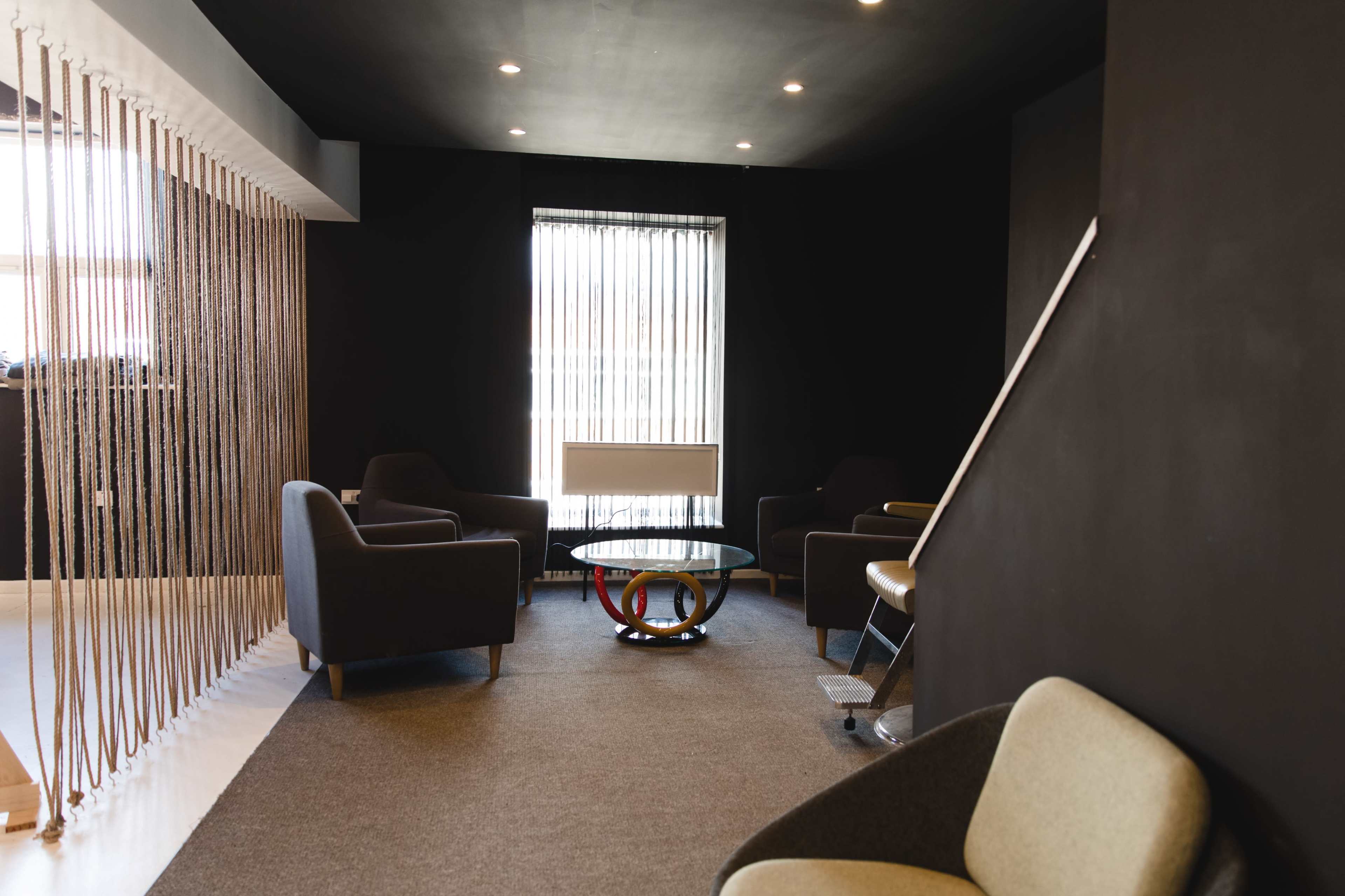 A modern lounge area with dark walls, a circular glass coffee table, and several upholstered chairs arranged around it.