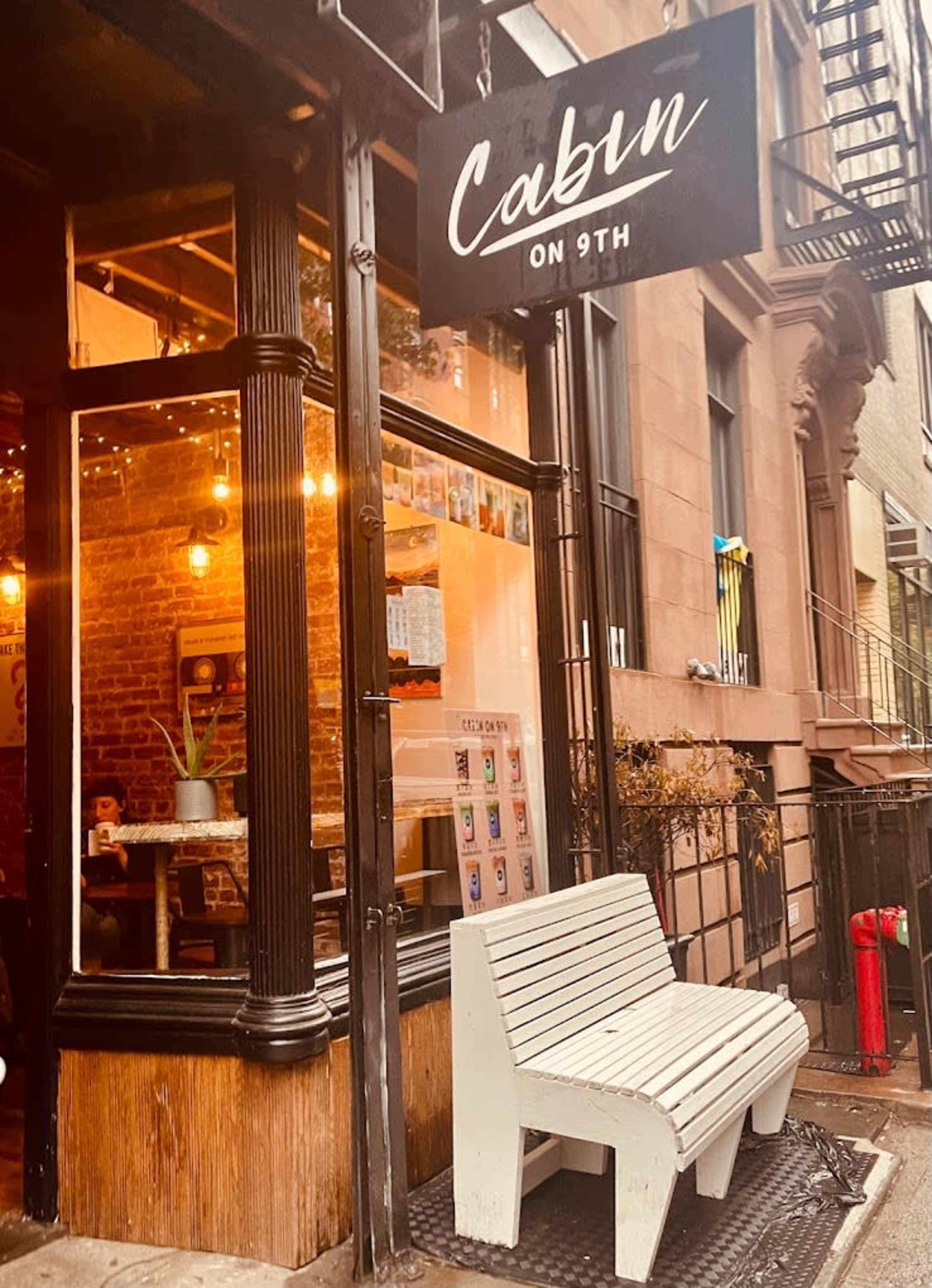 A café named "Cabin on 9th" with a large sign above the entrance, featuring a white wooden bench outside and warm, inviting lighting from within.