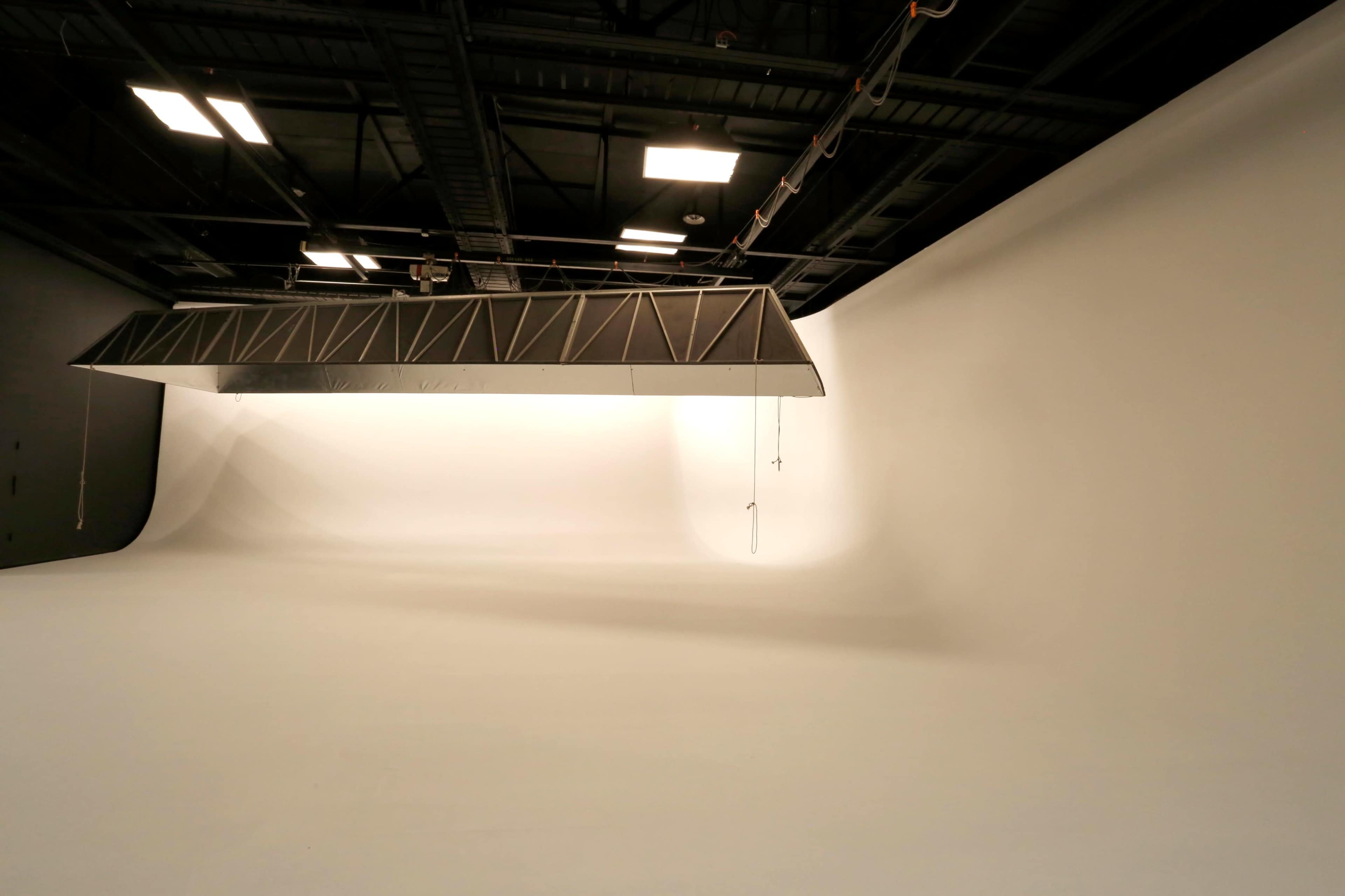 An empty photography studio with a large white backdrop and overhead lighting equipment.