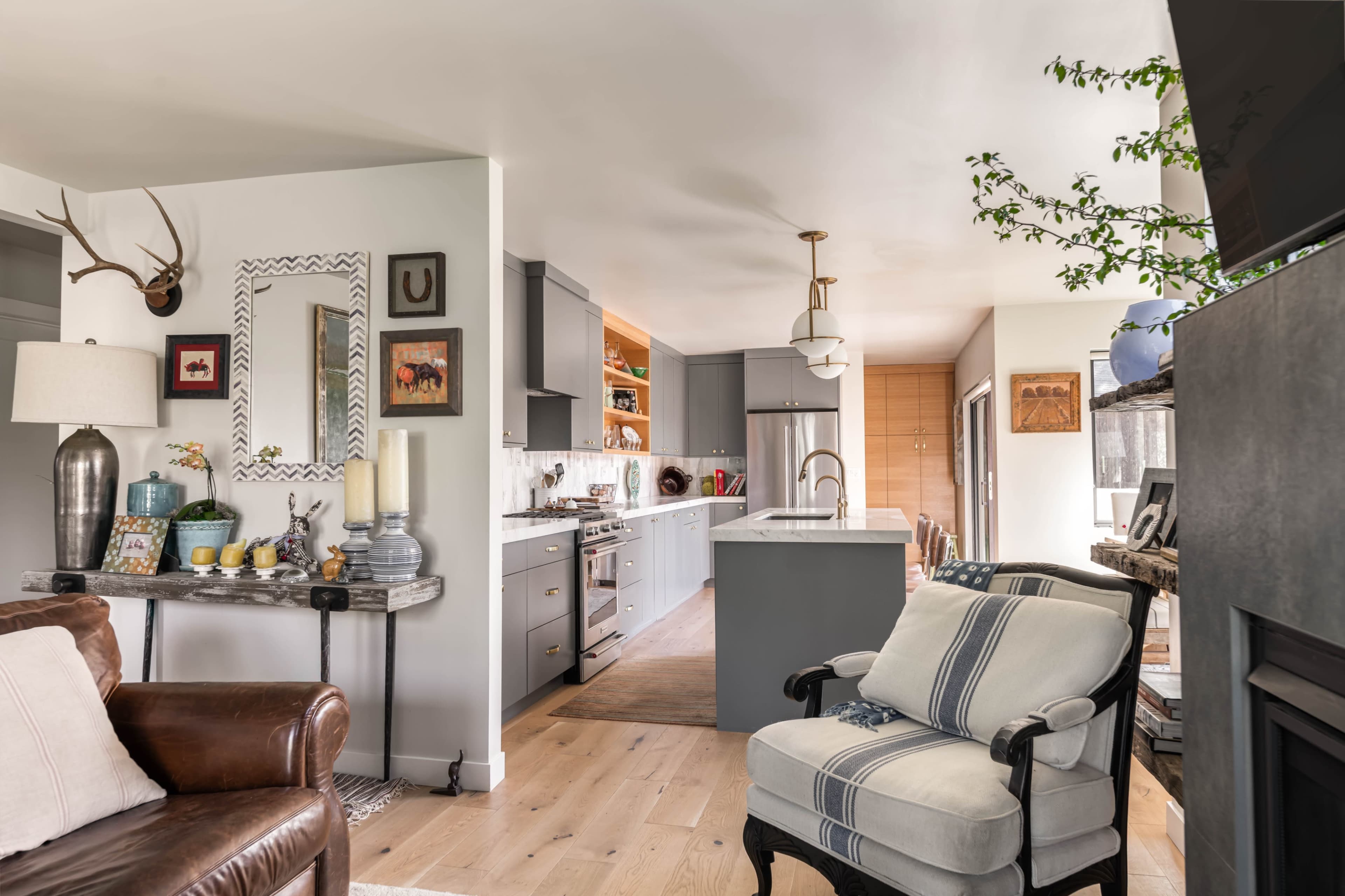 The image shows a modern open-concept kitchen and living room with a blend of light-colored cabinetry and wooden accents.