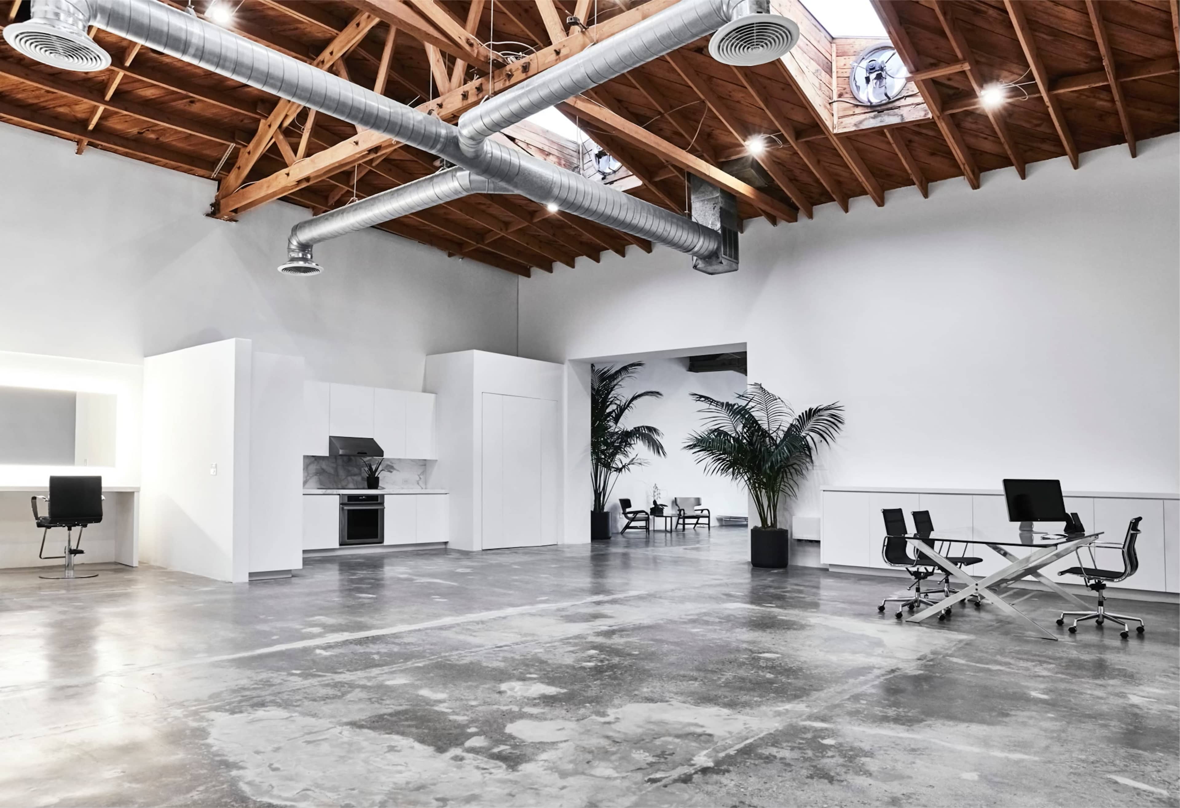 A spacious and minimalist office interior with wooden beams, gray concrete flooring, and various modern furniture pieces.