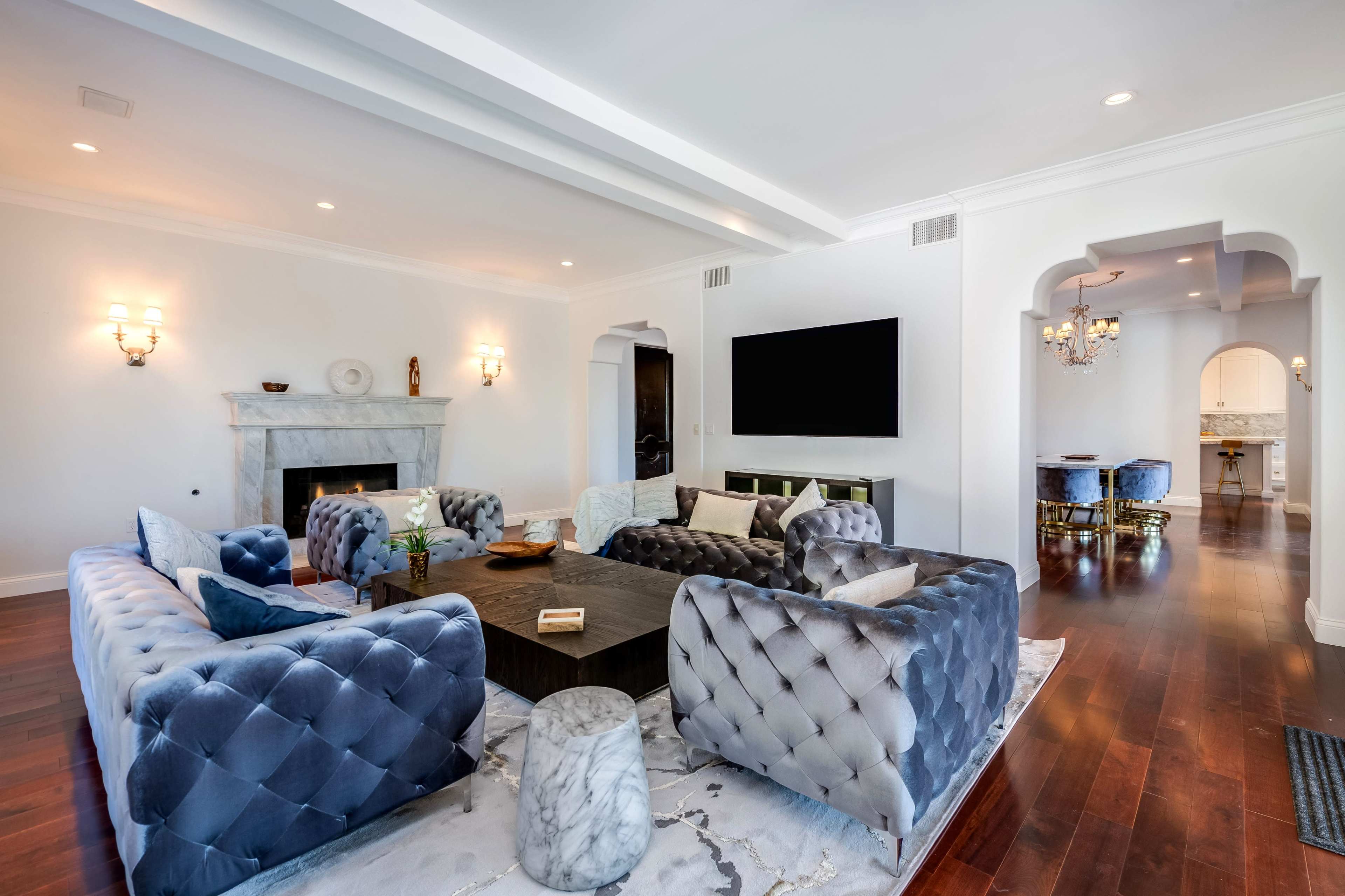 The image shows a spacious living room with a large, upholstered sectional sofa, a marble fireplace, and a flat-screen TV mounted on the wall.