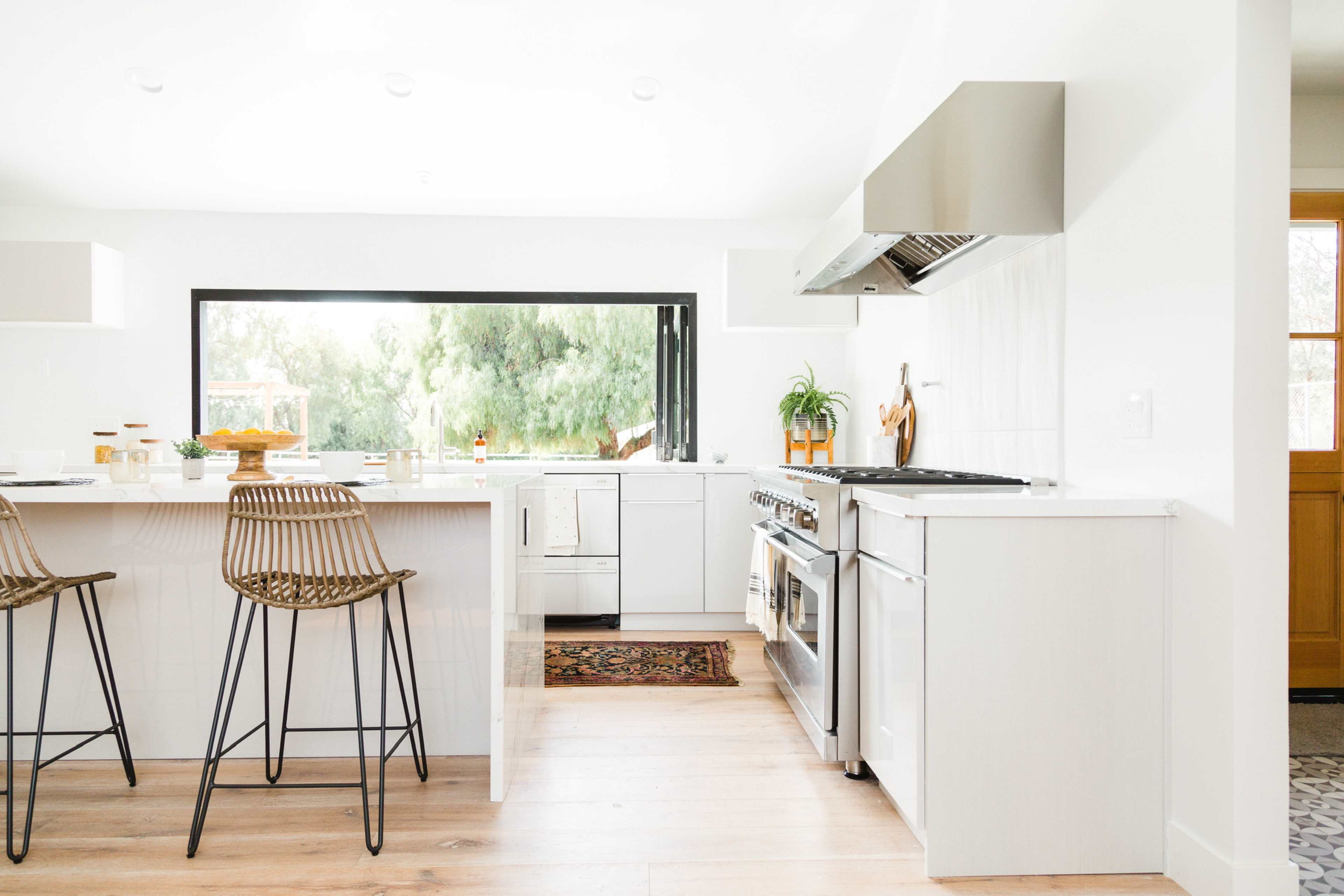 A modern kitchen features a large island with bar stools, stainless steel appliances, and a window that provides a view of greenery outside.