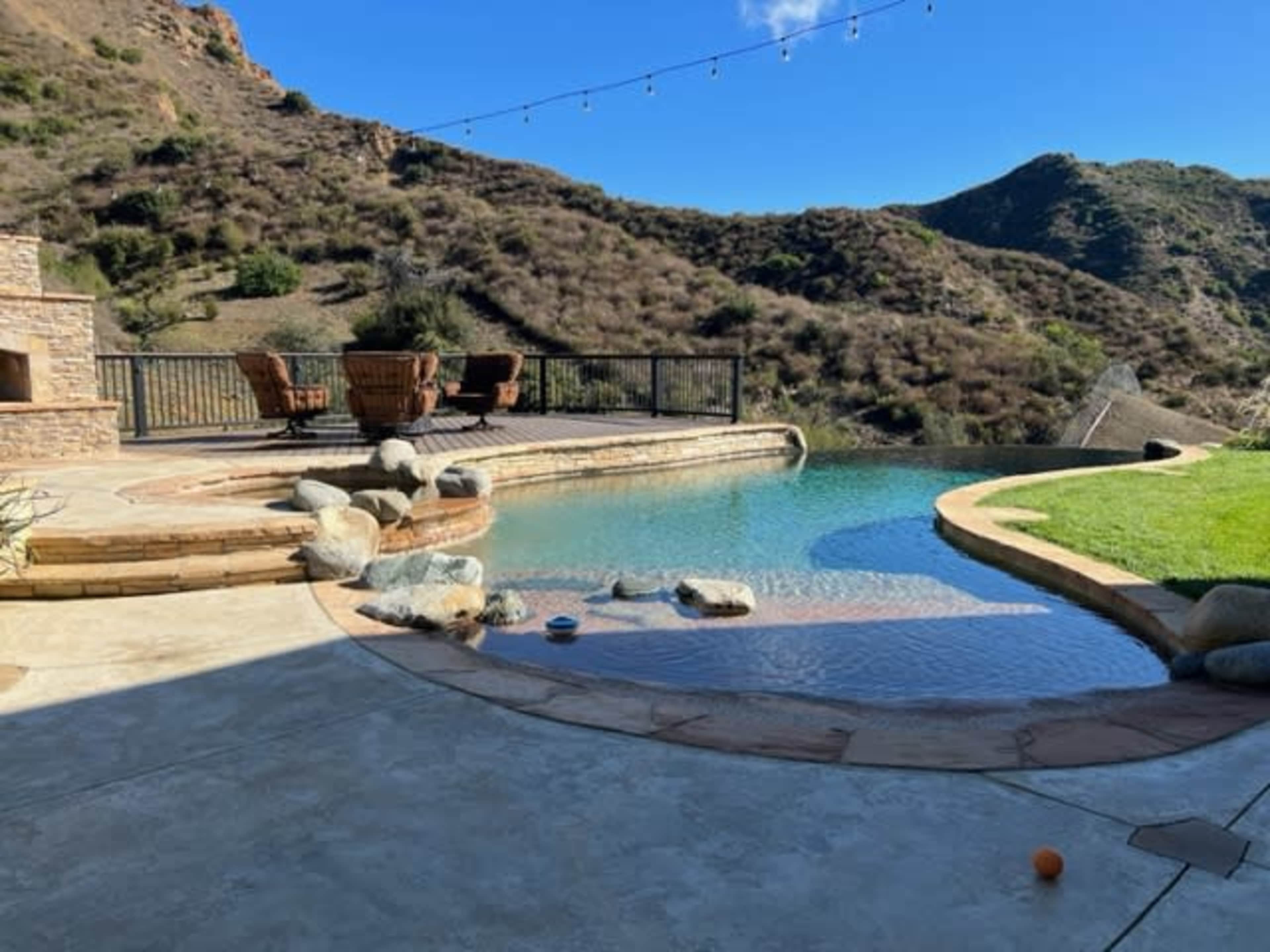 A backyard with a swimming pool, stone patio, and a view of rolling hills.
