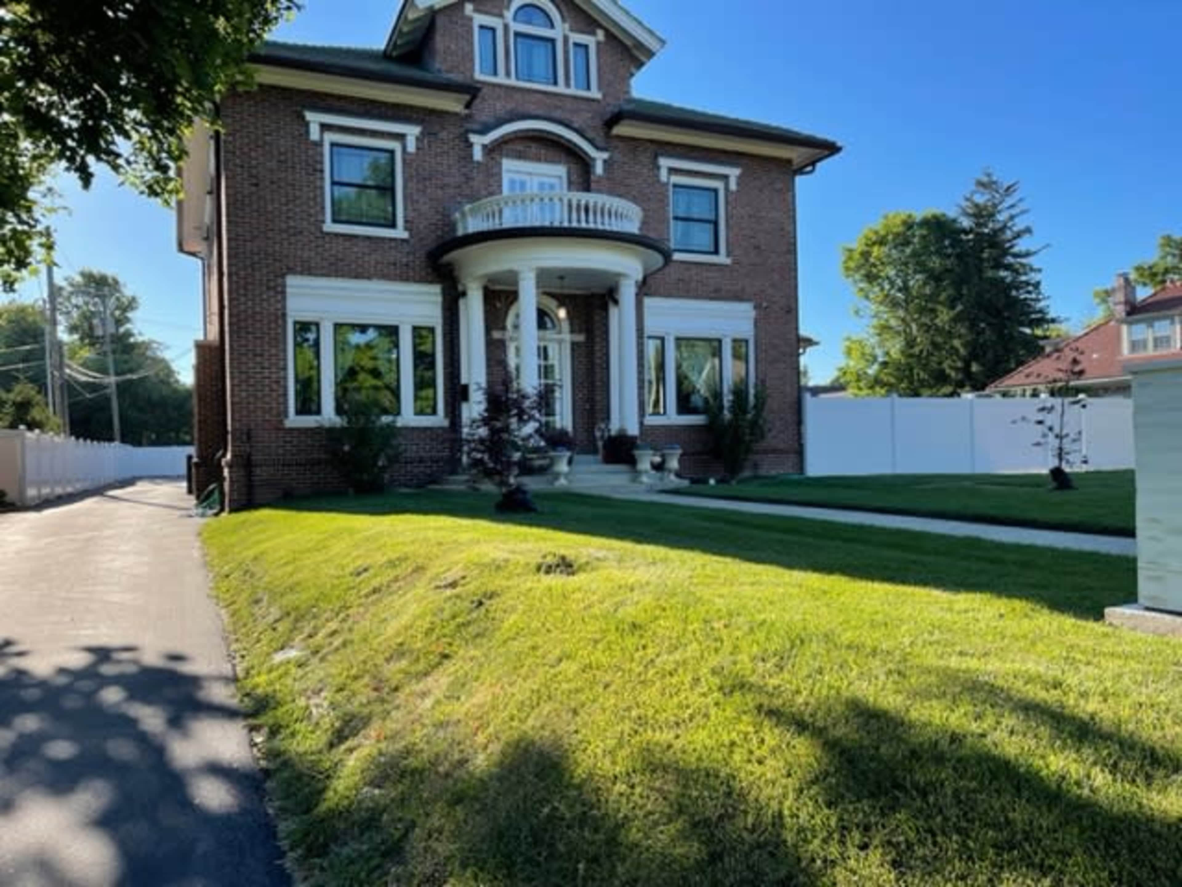 A large brick house with multiple windows and a front porch is surrounded by a neatly maintained lawn and a paved walkway.