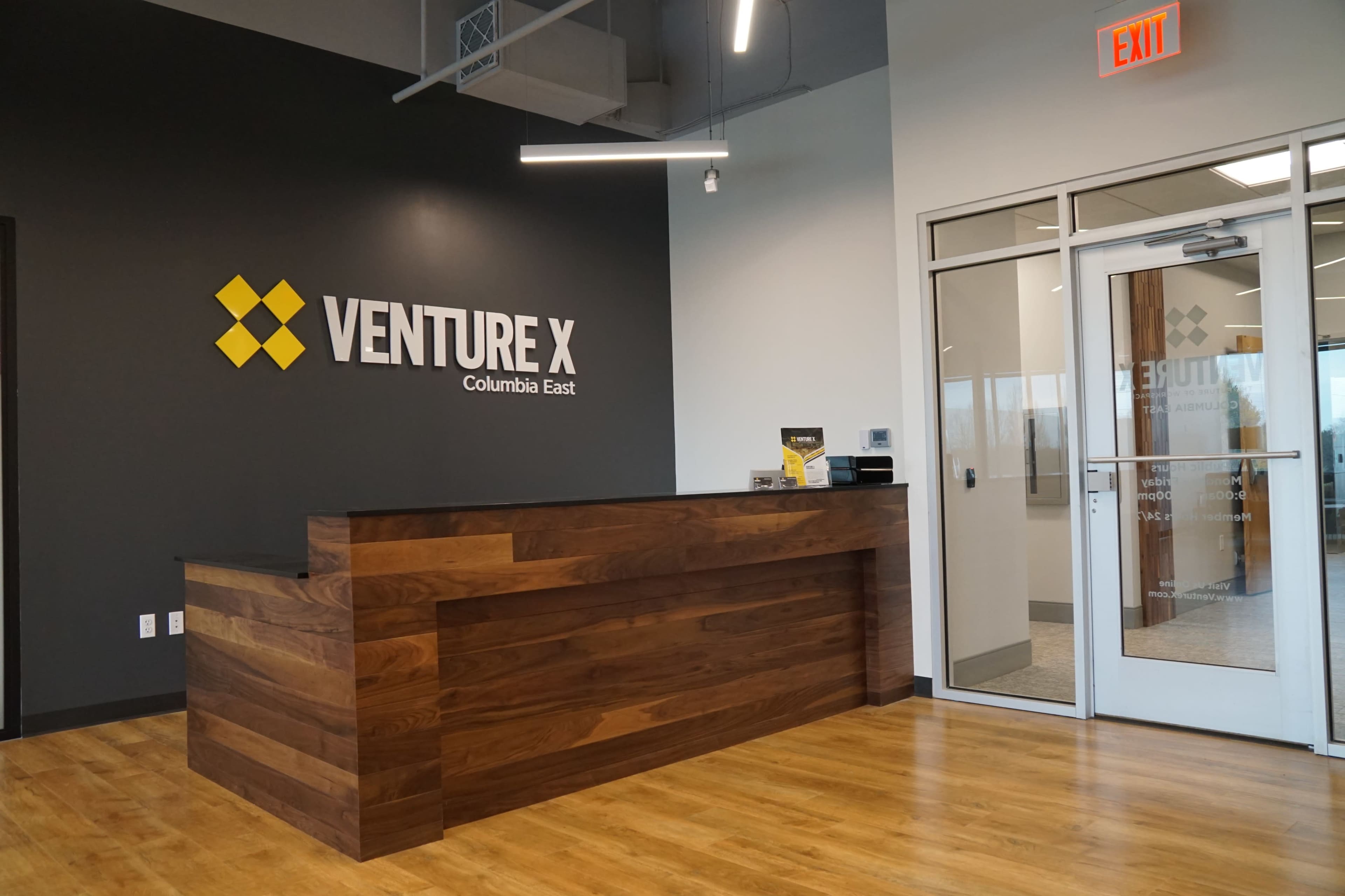A modern reception area with a wooden front desk and a wall featuring the "Venture X" logo.