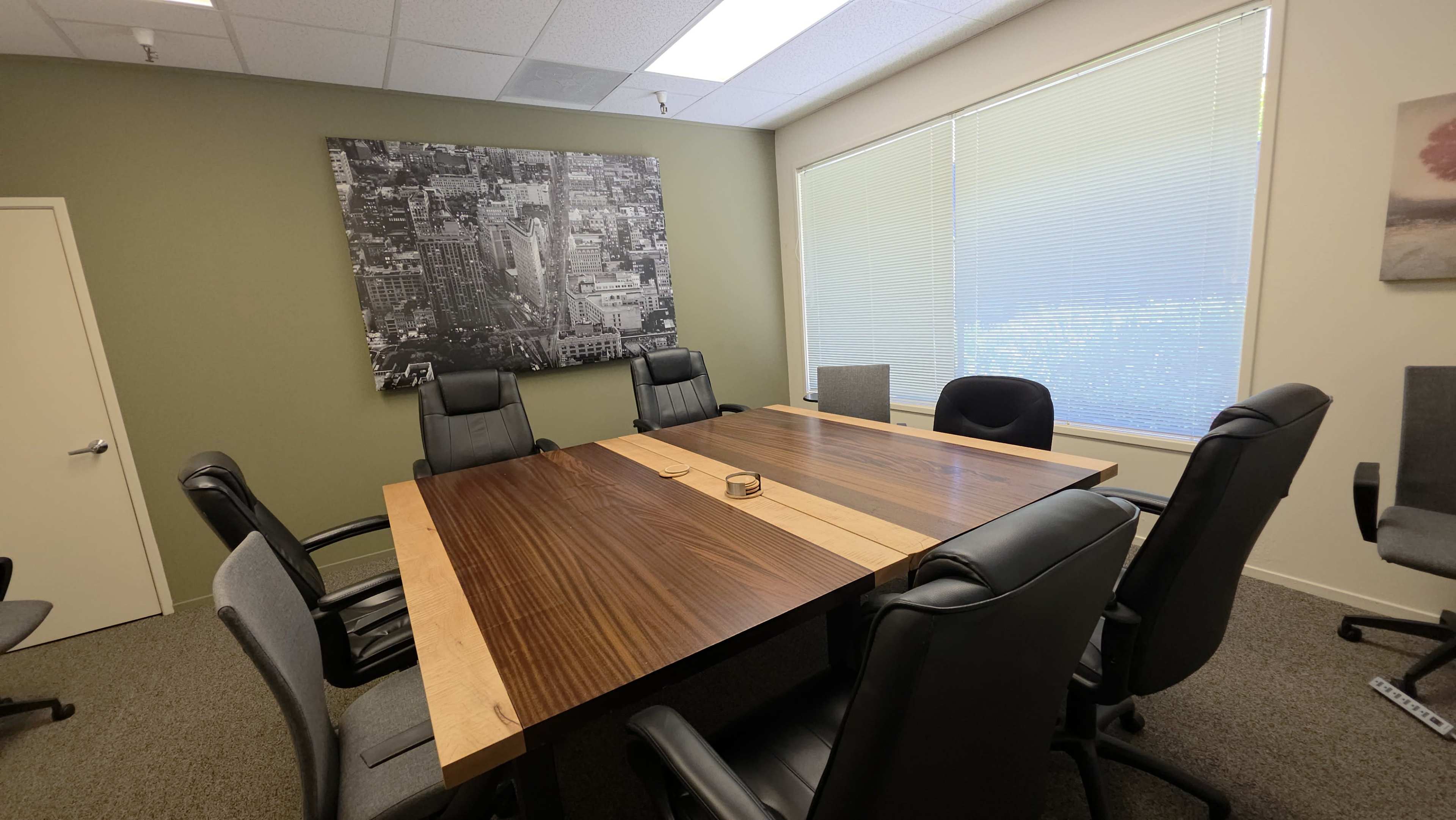 The image shows a conference room with a large wooden table surrounded by several office chairs, and a large black-and-white cityscape photograph on the wall.