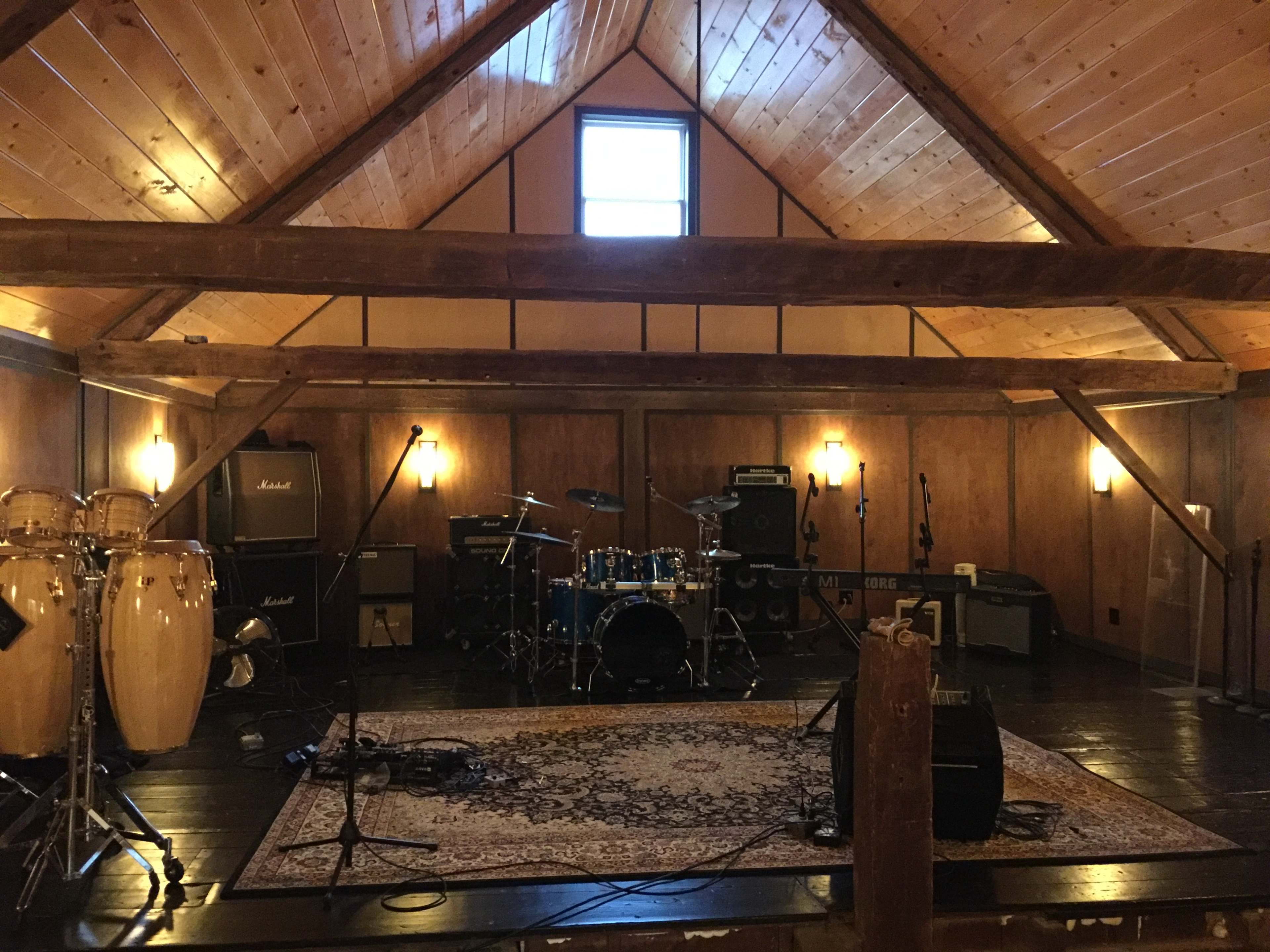 A wooden music studio with various instruments, including drums and percussion, positioned in a space with exposed beams and warm lighting.