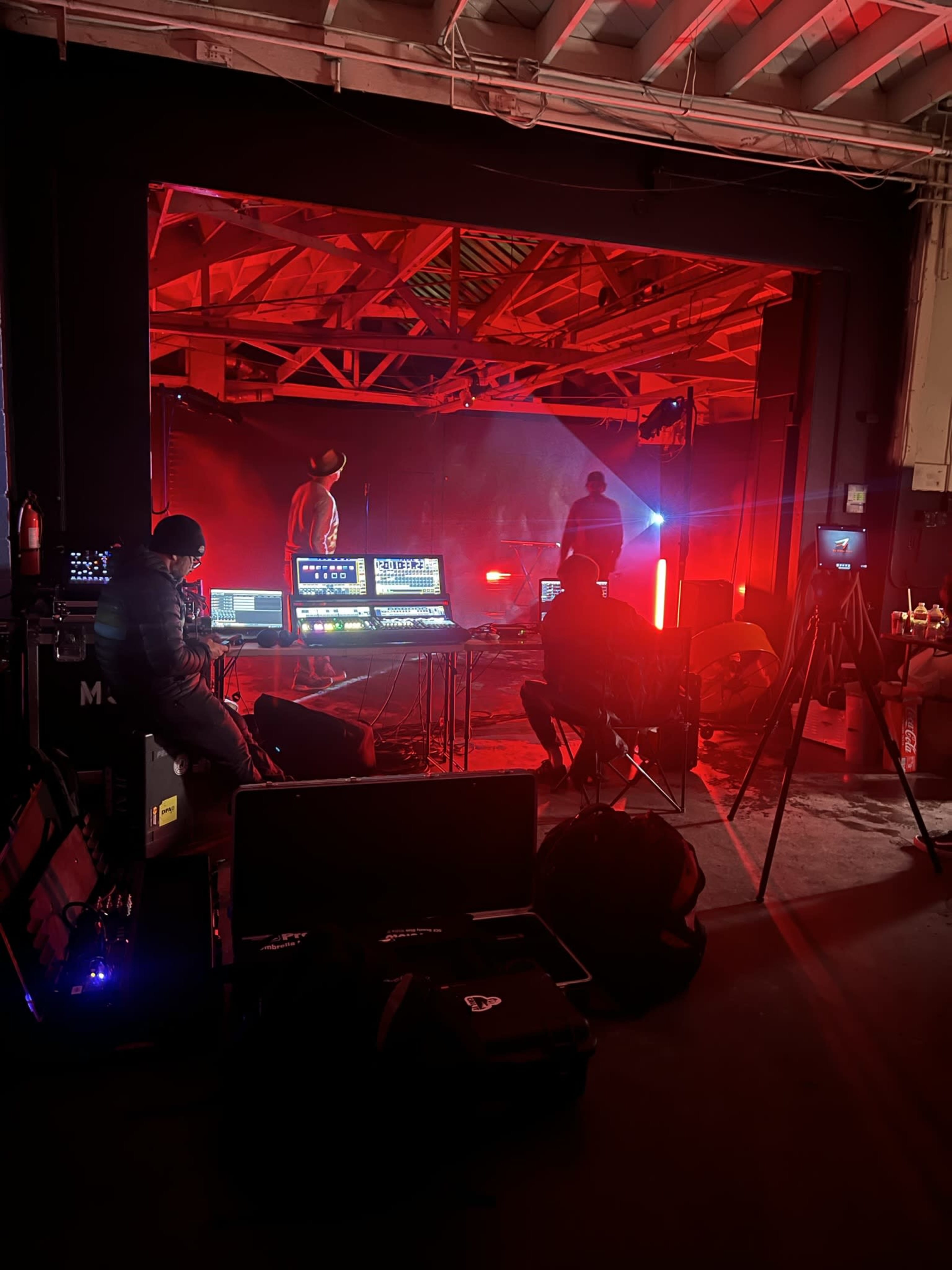 A group of technicians operates various equipment behind the scenes of a performance illuminated by red lights.