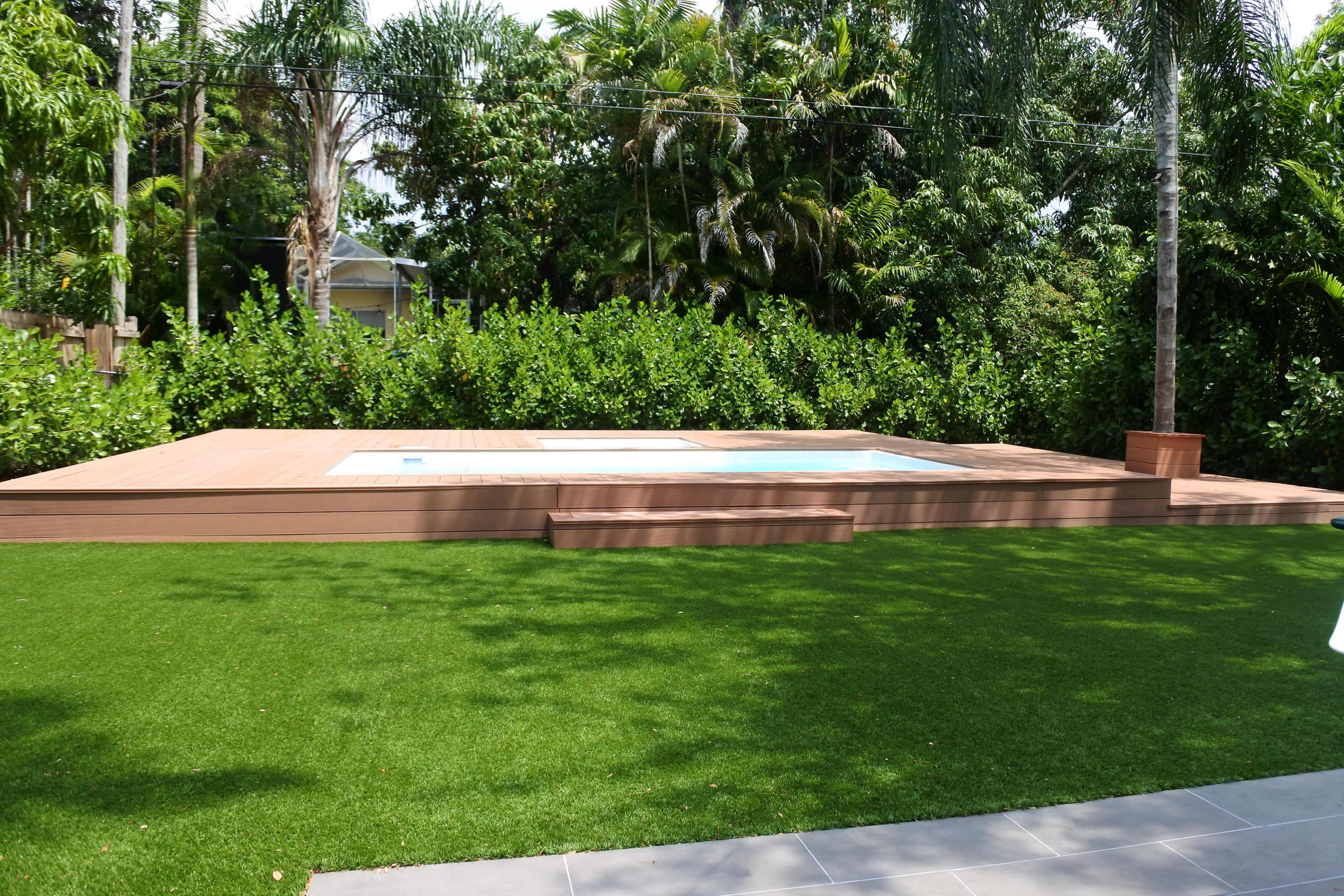 A wooden deck with two small swimming pools surrounded by artificial grass and tropical vegetation.