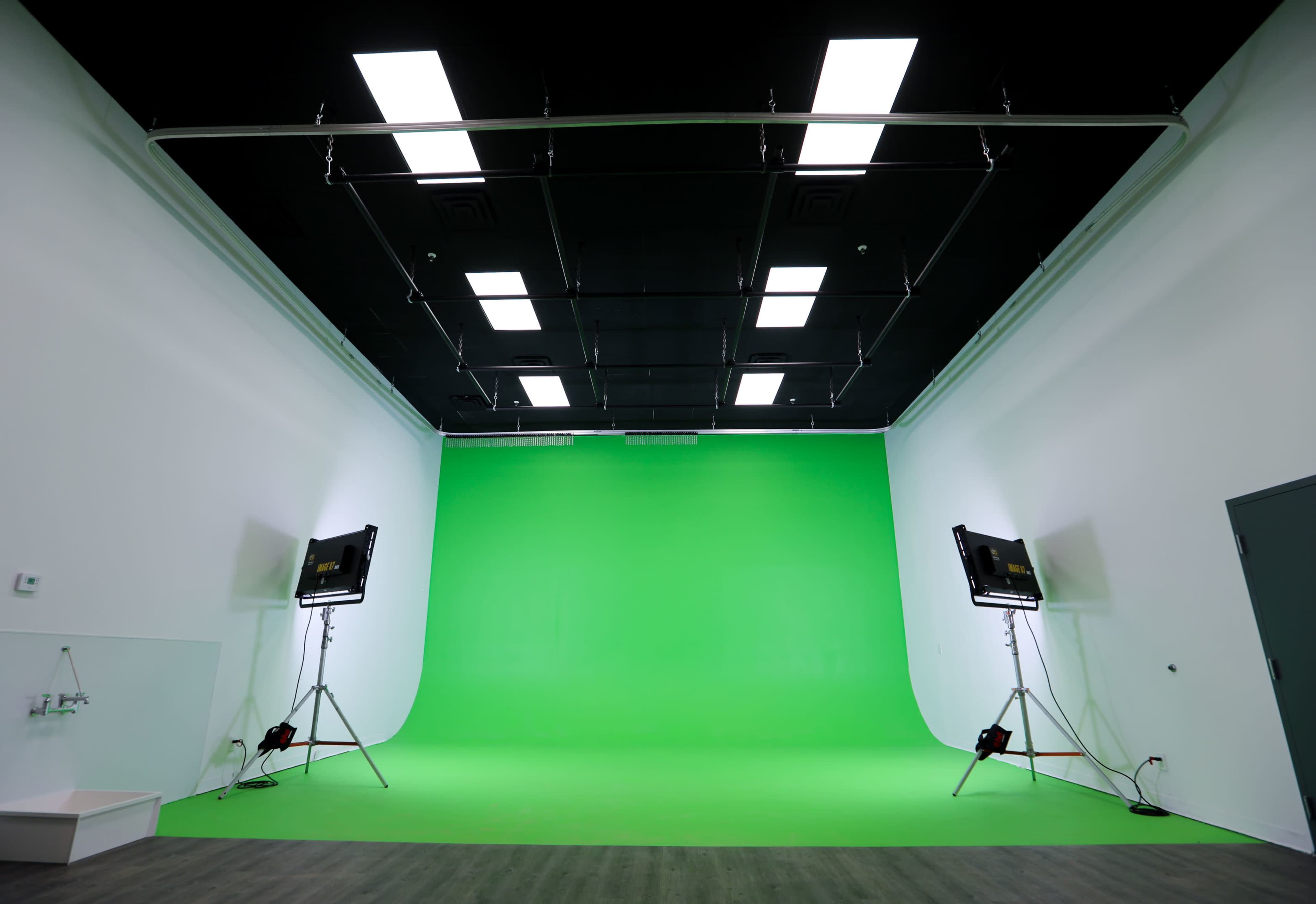 The image shows a large room with a bright green backdrop and lighting set up on stands.