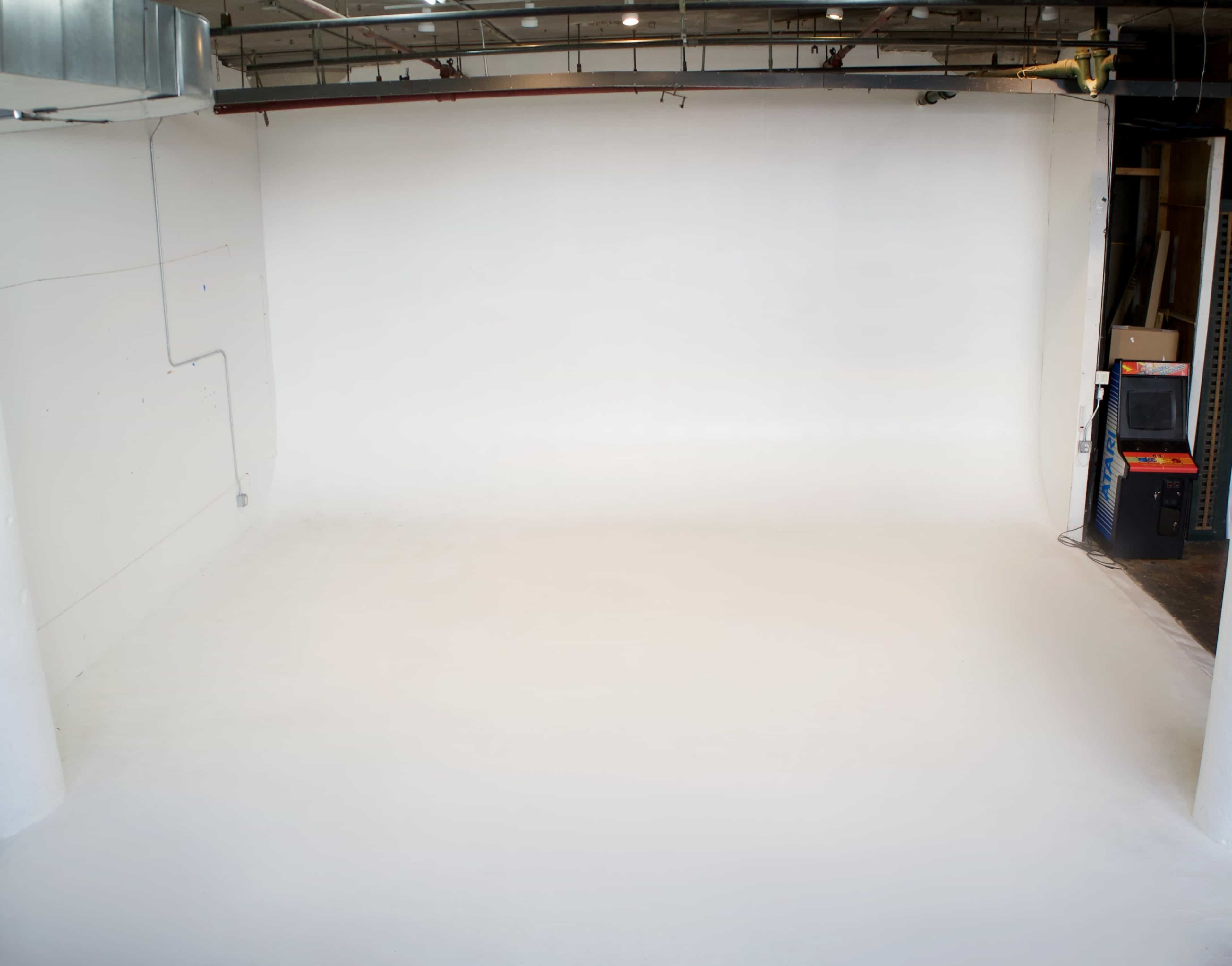 The image shows a large, empty studio space with white walls and a smooth white floor.