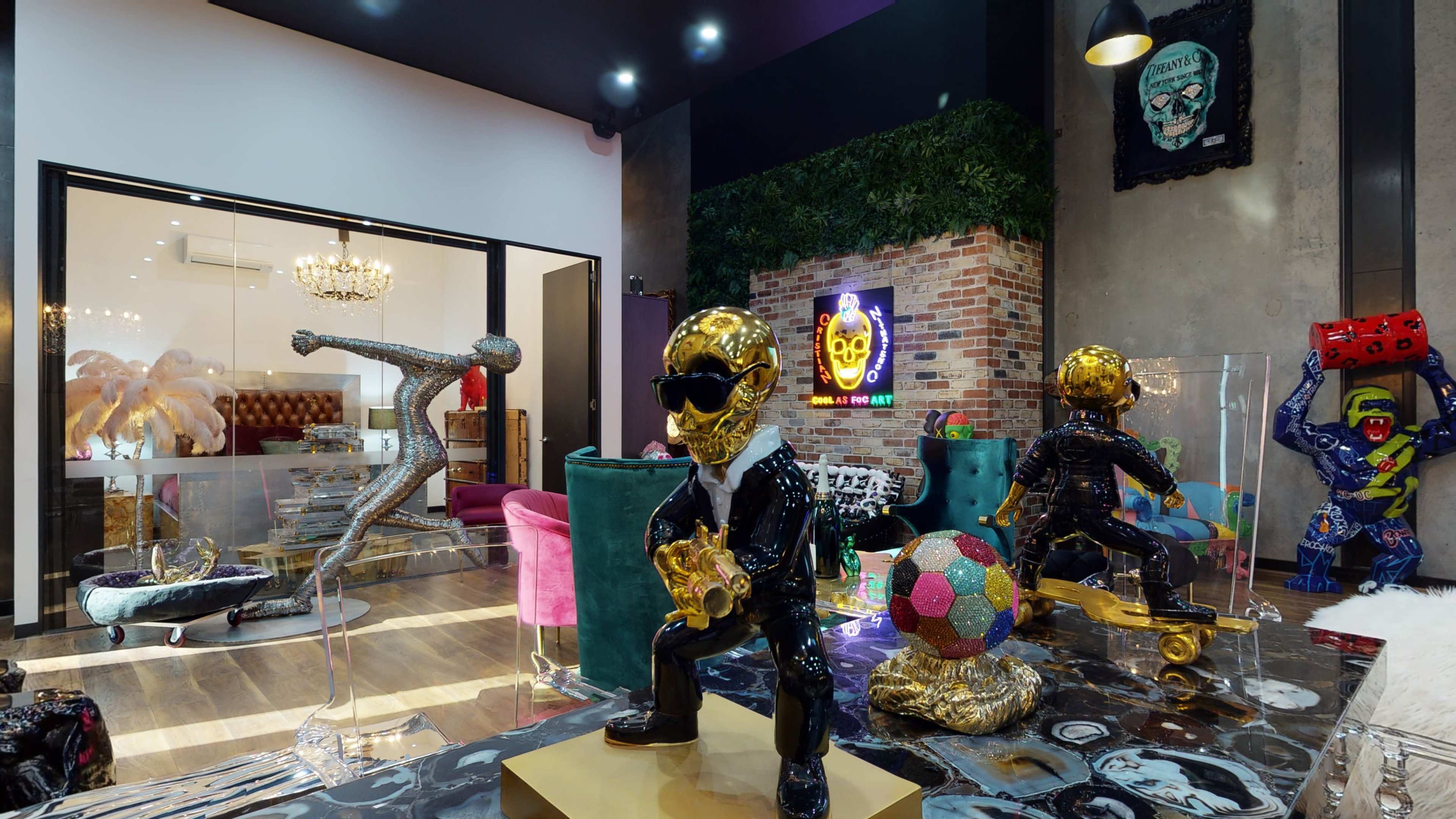The image showcases a modern gallery space featuring vibrant art pieces, including gold-skull sculptures and colorful furniture against a textured wall backdrop.