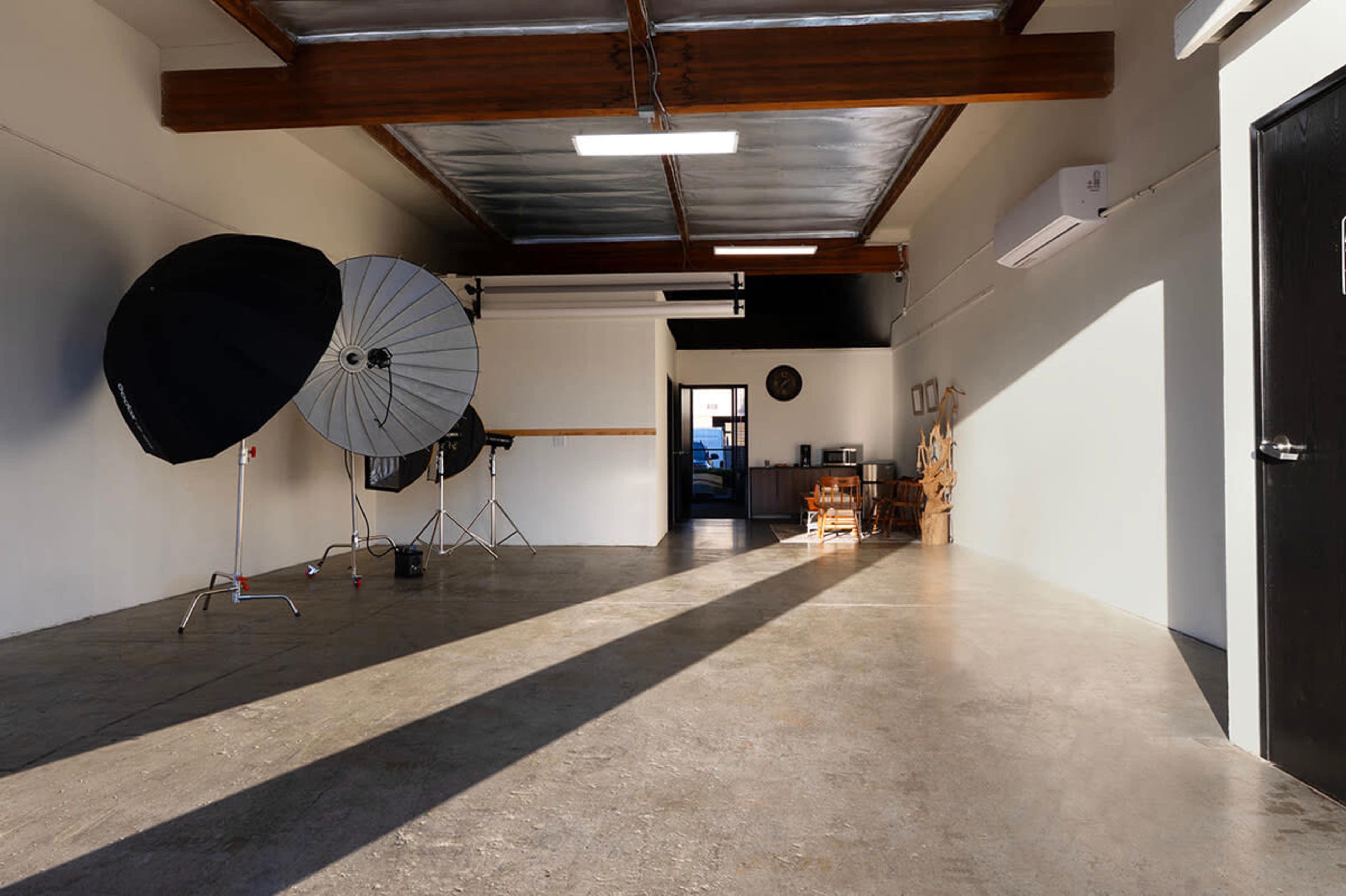 The image shows a spacious, well-lit studio with photography equipment and a desk visible in the background.