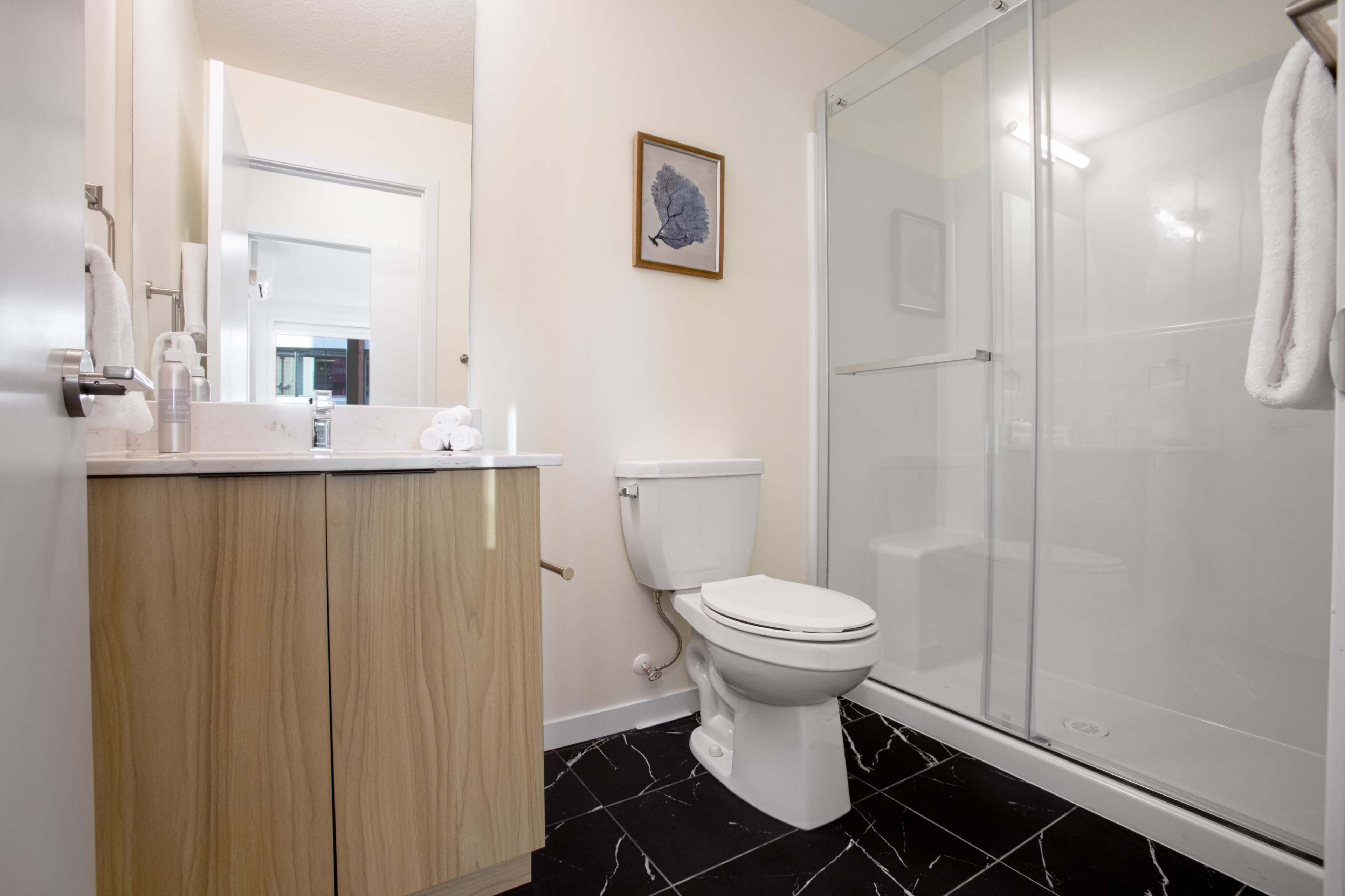 A modern bathroom featuring a glass shower, a toilet, a wooden vanity with a sink, and a framed artwork on the wall.