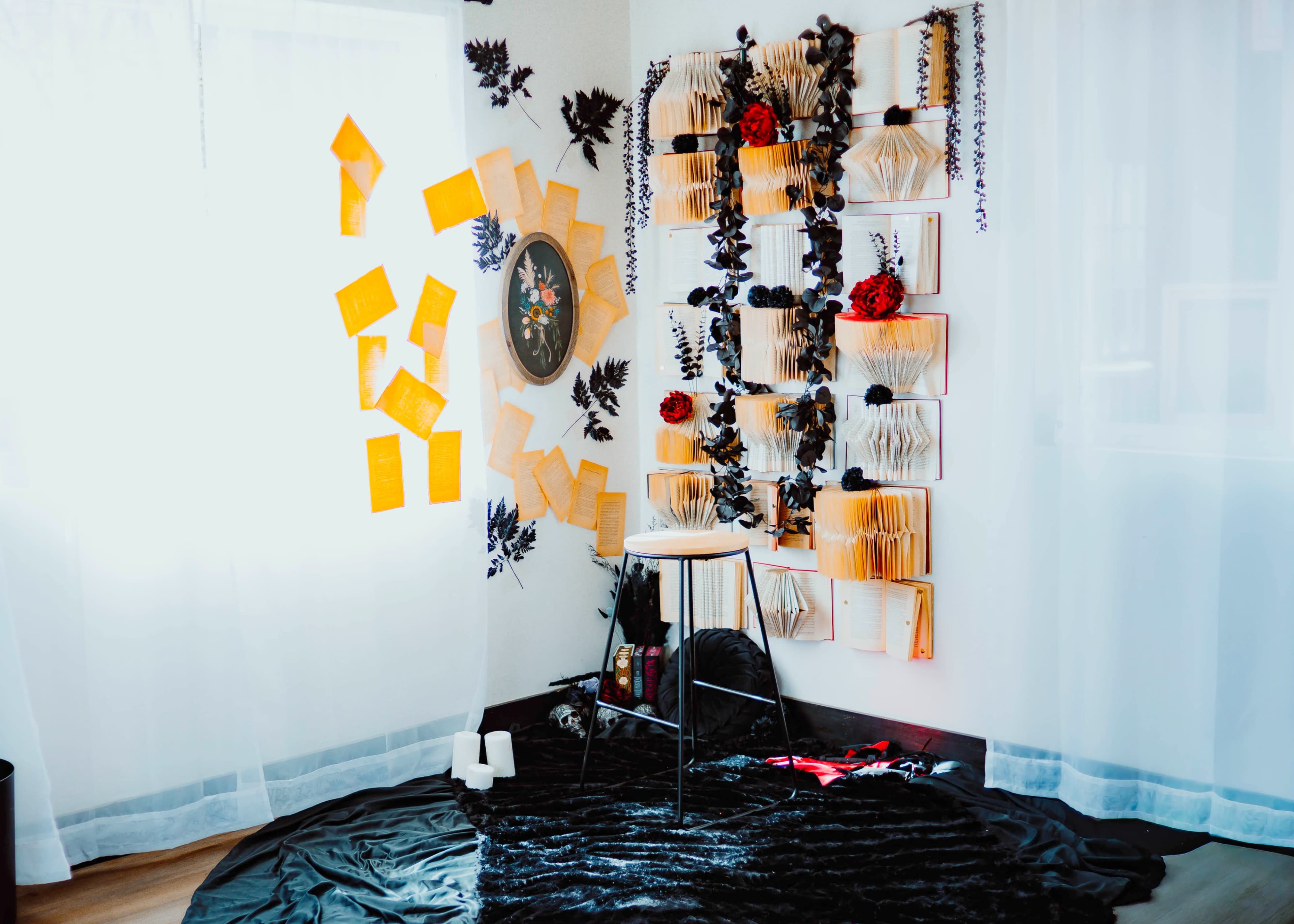 The image shows a room with a black rug, a white stool, and a wall decorated with orange notes, a circular frame, and book-like decorations adorned with flowers.