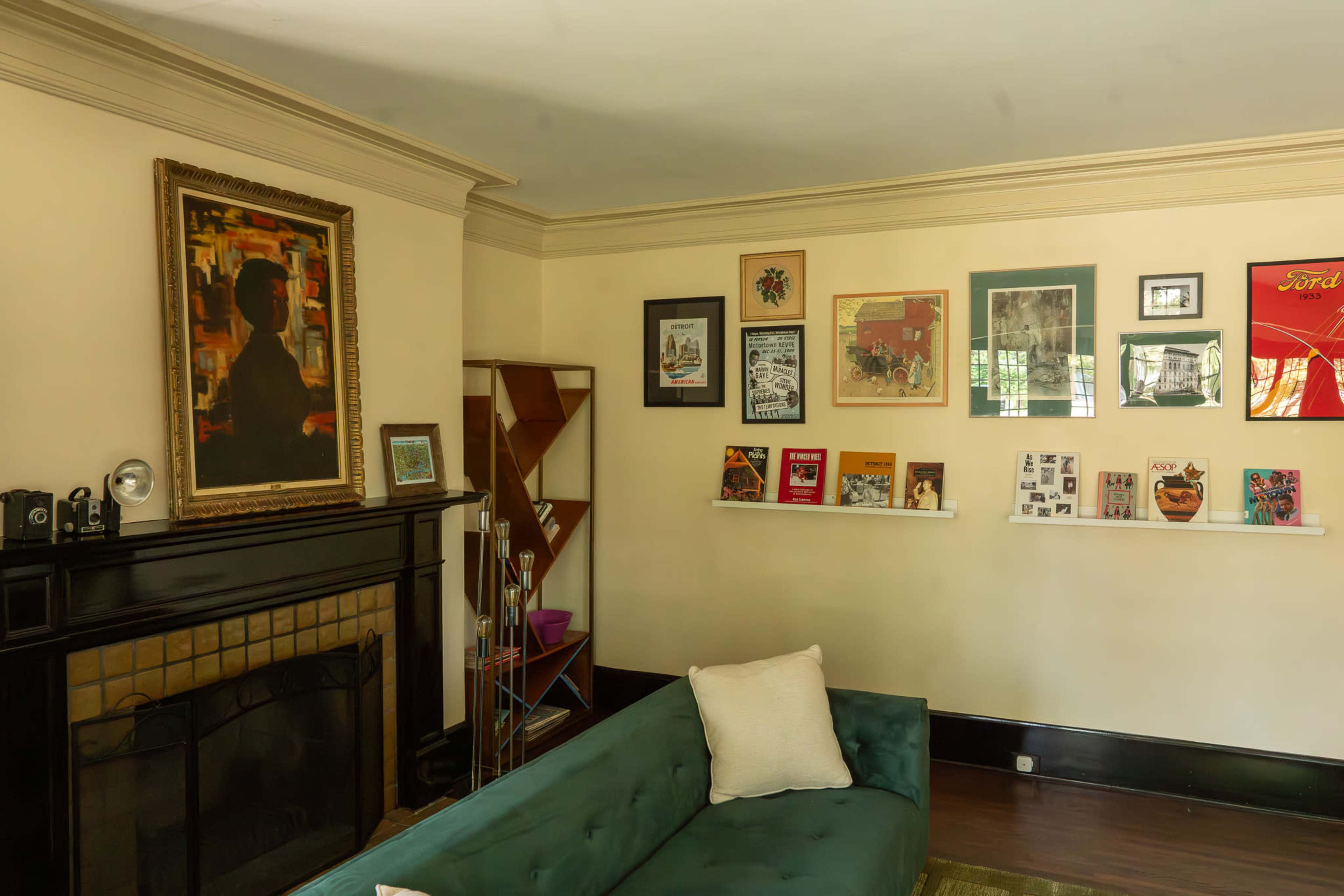The image shows a living room with a green couch, framed artwork on the walls, and a mantelpiece featuring a camera and decorative items.