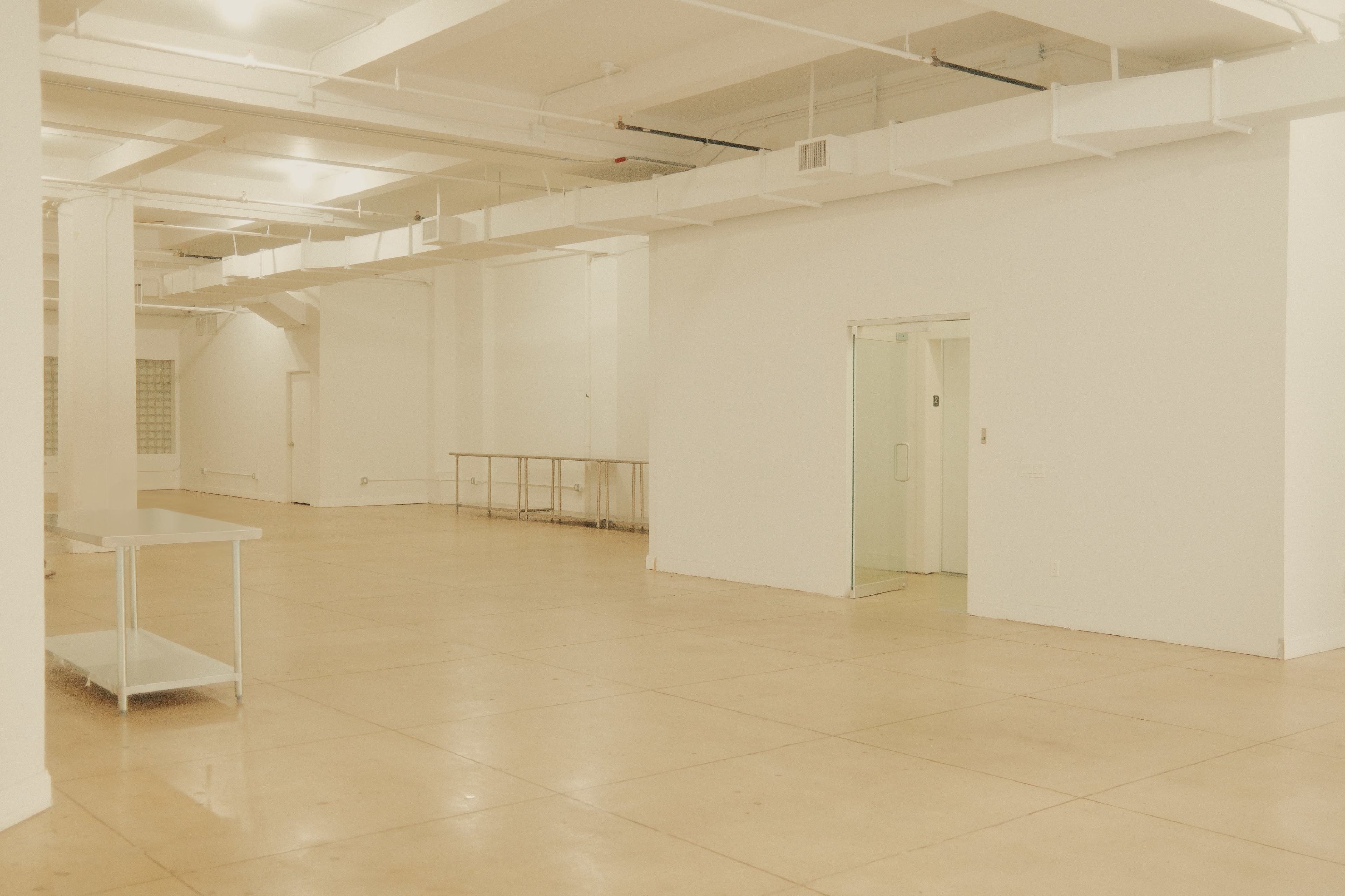 The image shows a large, empty room with white walls, a polished concrete floor, and minimal furnishings.