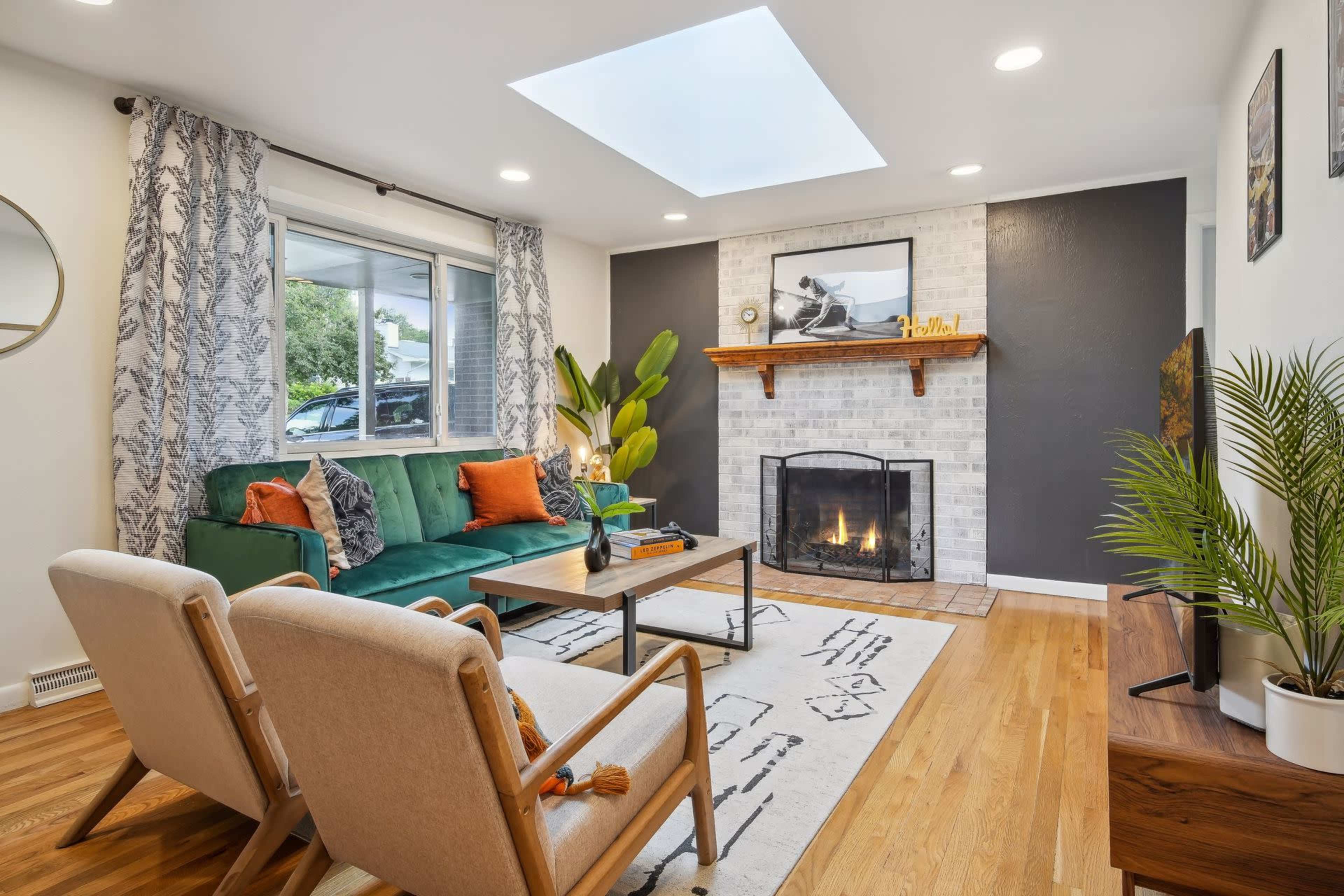 The living room features a green sofa, two armchairs, a coffee table, a fireplace with a brick surround, and a skylight overhead.